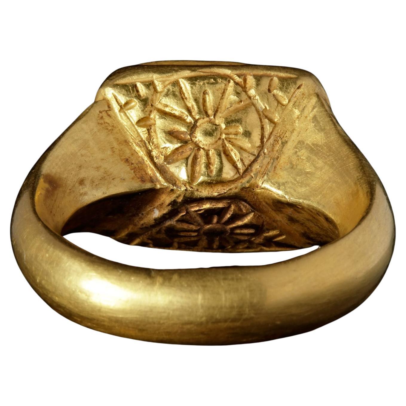 A Byzantine gold ring made of repousse sheet with a square topaz intaglio showing the bust of Christ with a cross shaped nimbus. The ring itself is made of thin, but robust, gold sheet with the underside of the shank decorated with flowers.
27 by 24