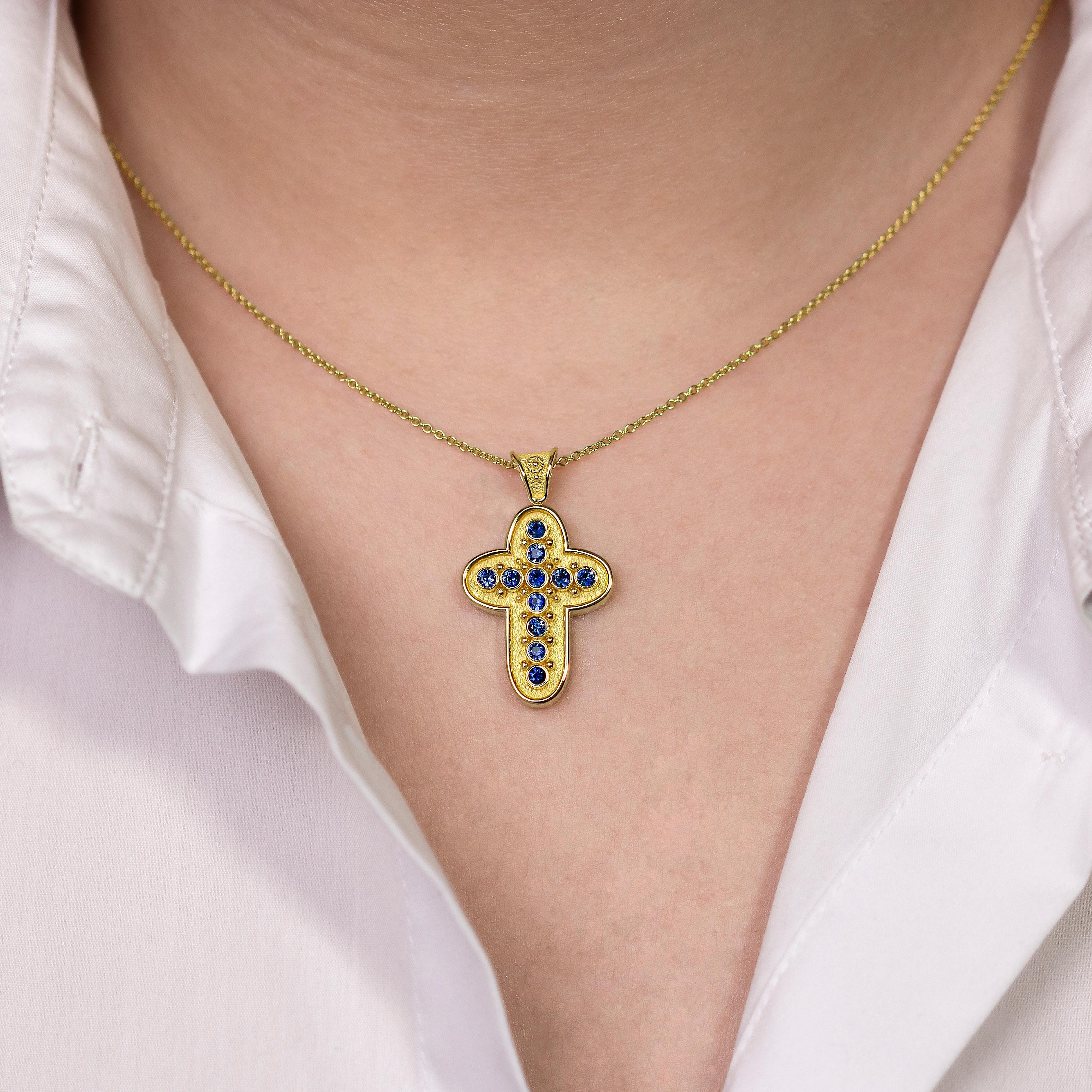 Enhance your allure with a gold cross pendant adorned with radiant round sapphires and intricate granulation details. This masterpiece is a testament to timeless beauty and unparalleled craftsmanship, adding a touch of sophistication to your style.