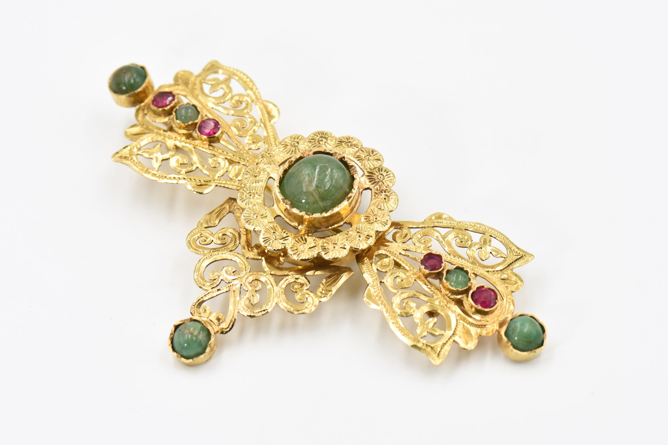 Dramatic 18k yellow gold filagree bow brooch pendant featuring a leaf and scroll design accented with cabochon emerald and man made faceted rubies.  The back has a 