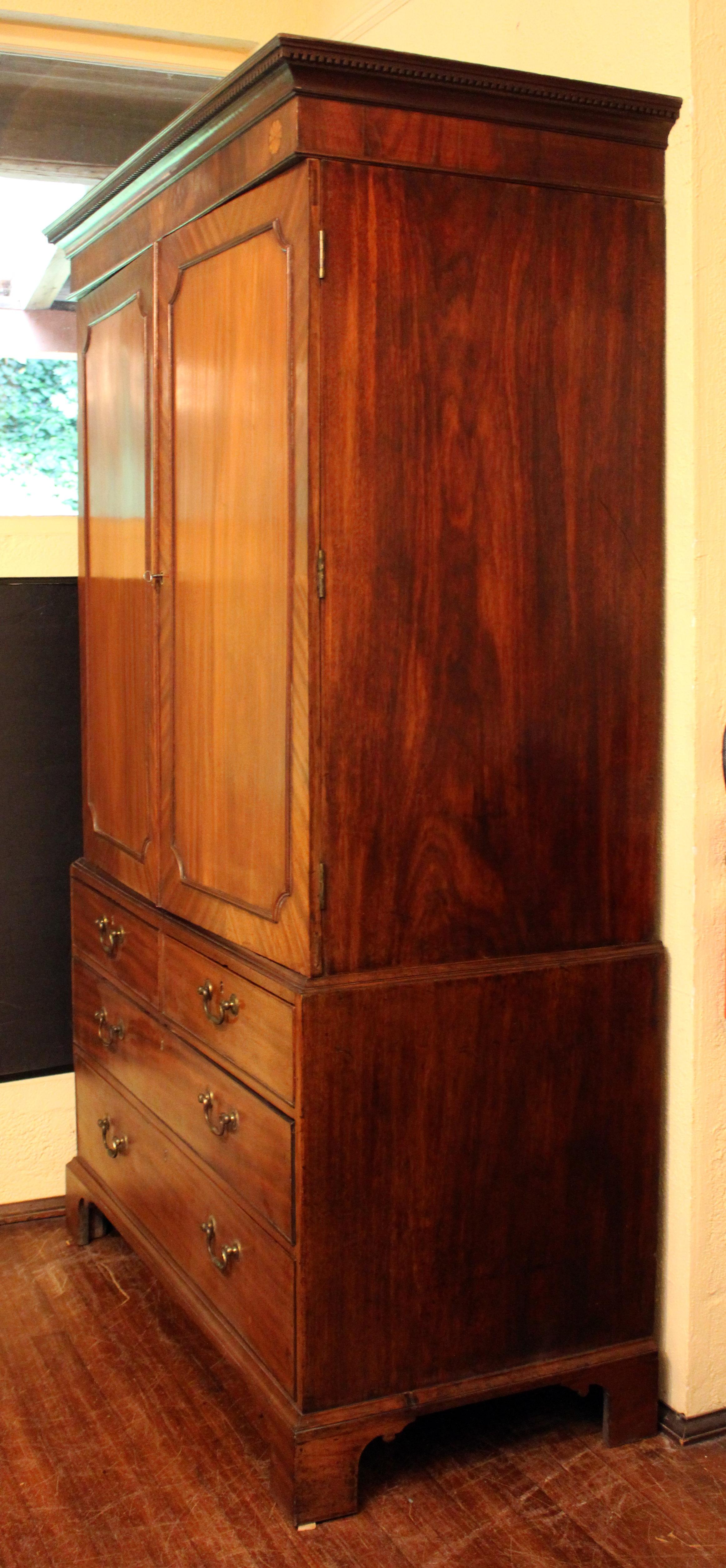 Circa 1780 Georgian period linen press, English. Choice solid mahogany & mahogany veneers. Cavetto molded corner paneled triple hinged doors. The crown featuring paterae inlays of satinwood & stained sycamore with a dentil & circle carved molding.