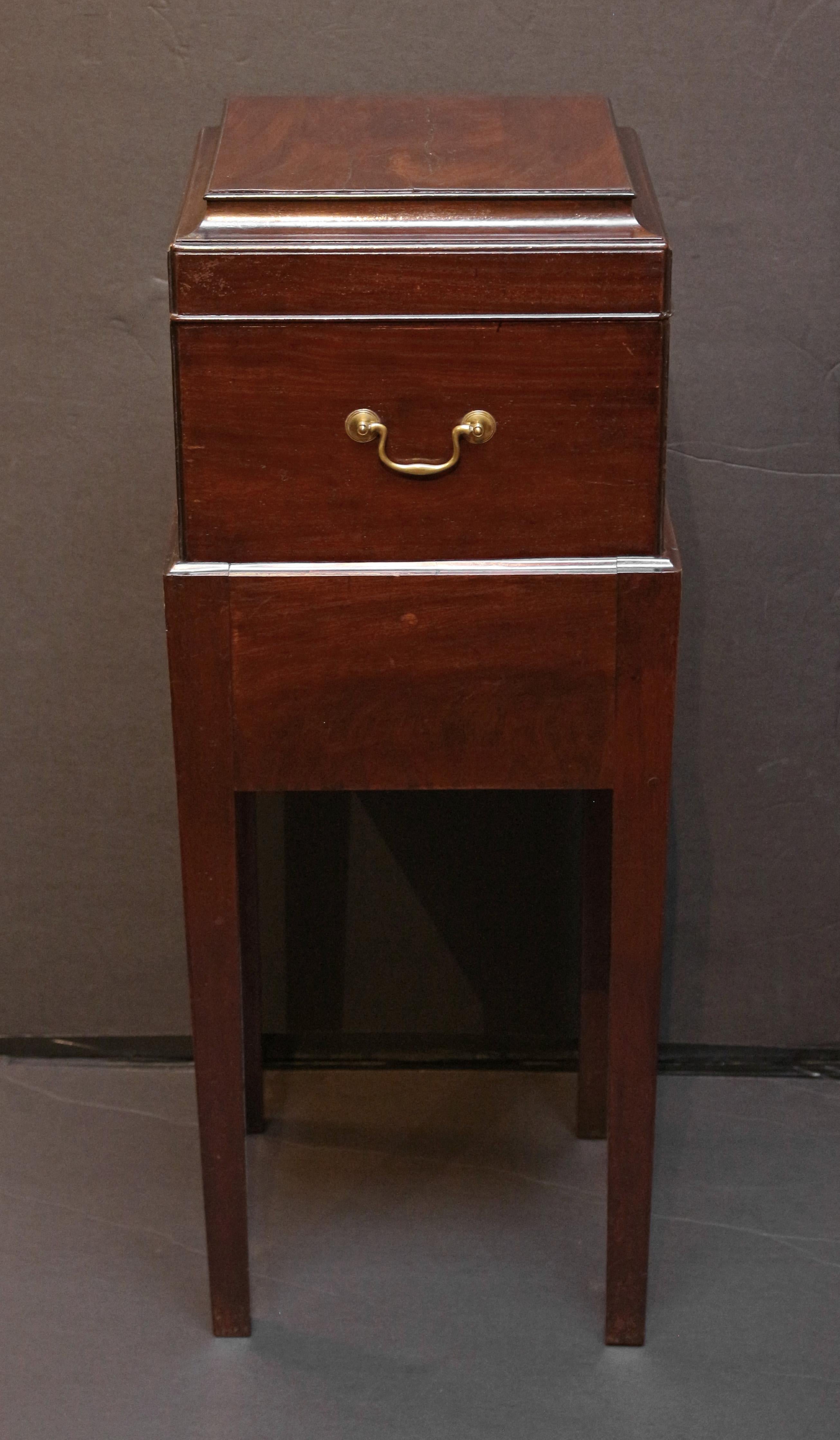 Circa 1780 George III period cellarette on stand, English. Mahogany & mahogany veneered cellarette, the stand with oak secondary wood. Useful drawer in the stand, raised on square, tapered legs. Boxwood escutcheons. Bail & rosette handles. Cove
