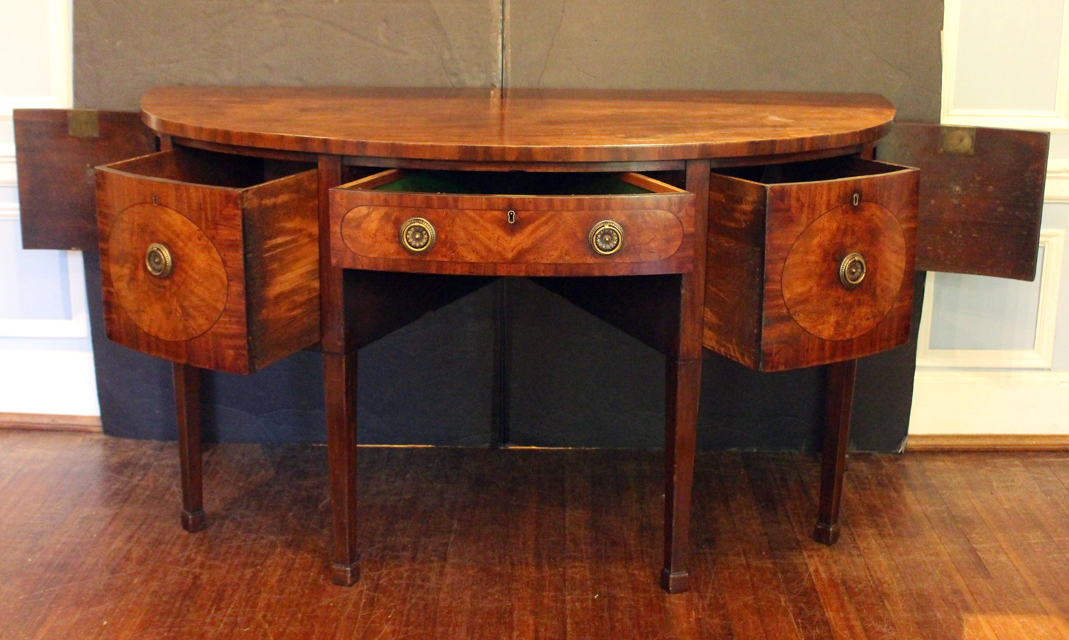 Circa 1790 Buffet démilune d'époque George III, anglais. Acajou et placages d'acajou avec chêne et bois secondaires. Elle repose sur des pieds carrés et fuselés avec des pieds Marlborough. Un tiroir doublé de feutre pour l'argenterie au-dessus de