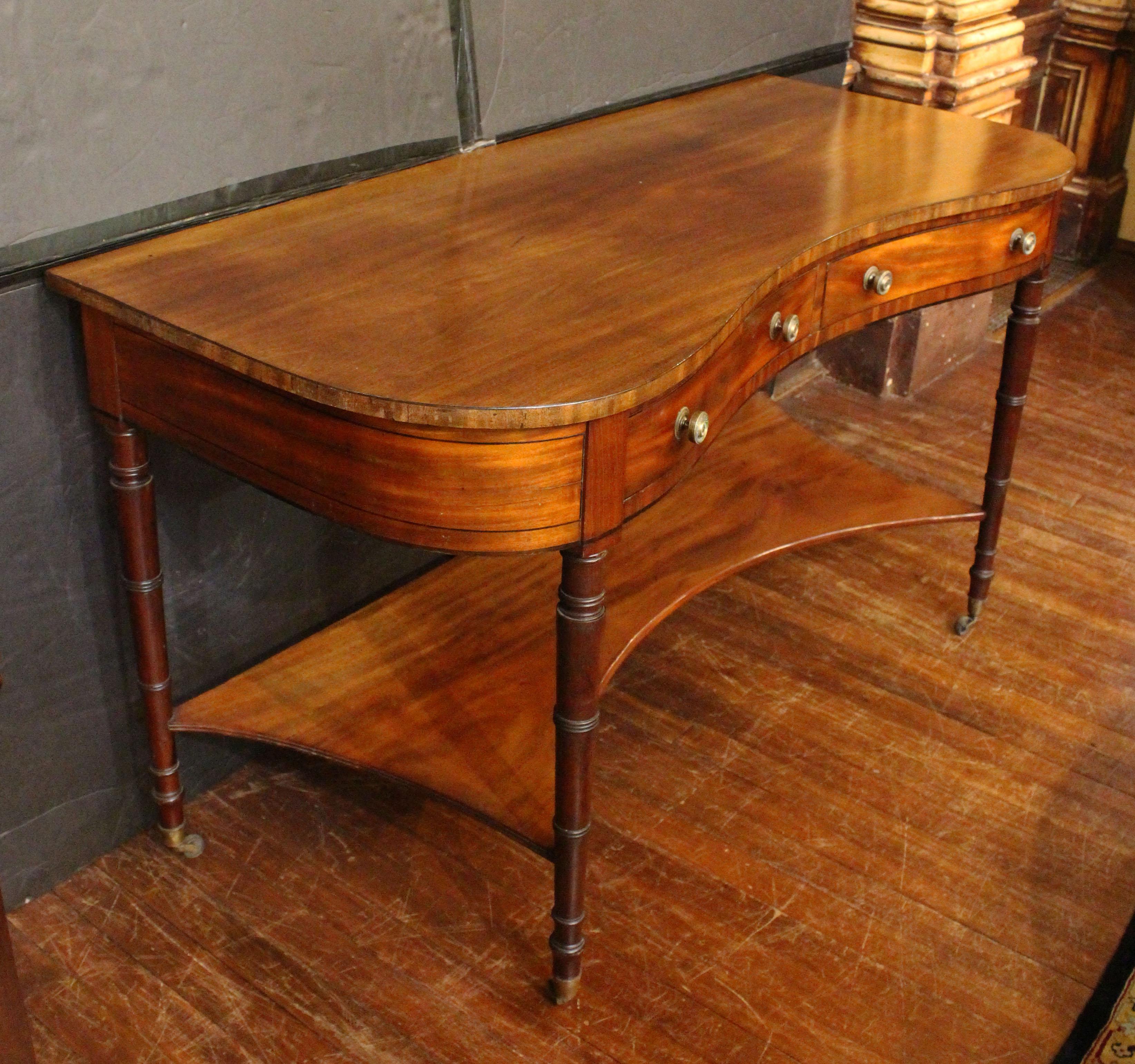 Circa 1810 Table de service à la manière de Sheraton, anglais. George III, époque Regency. Elegante forme d'arc-en-ciel. Pieds fuselés tournés en anneau se terminant par des coupelles et des roulettes en laiton. Placages d'acajou et d'acajou riches