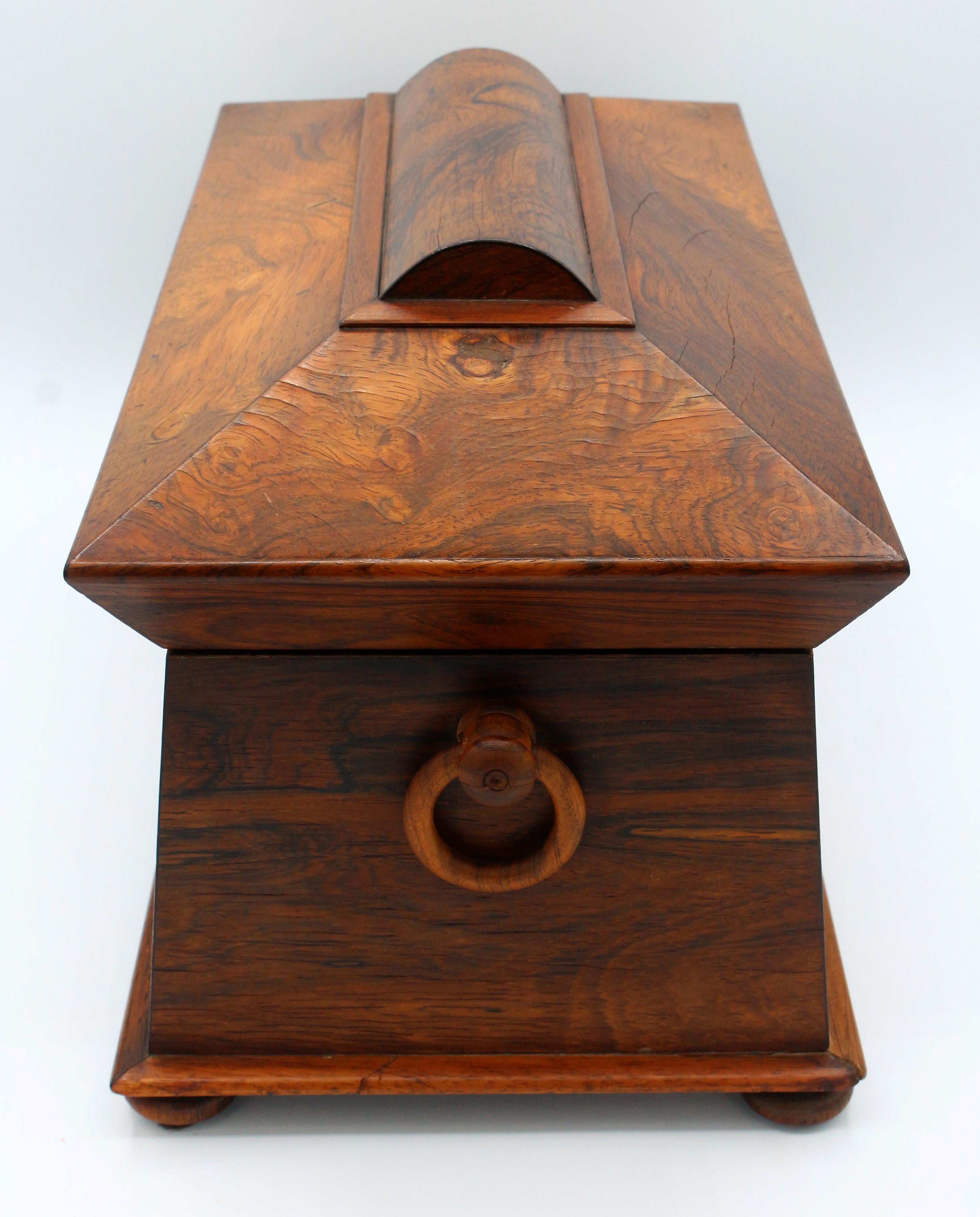 William IV period sarcophagus form tea caddy, English, circa 1830. Original interior fitted with a pair of dome-top tea canisters and section for sugar bowl (bowl lacking). Original treen ring handles & button feet.
13 5/8