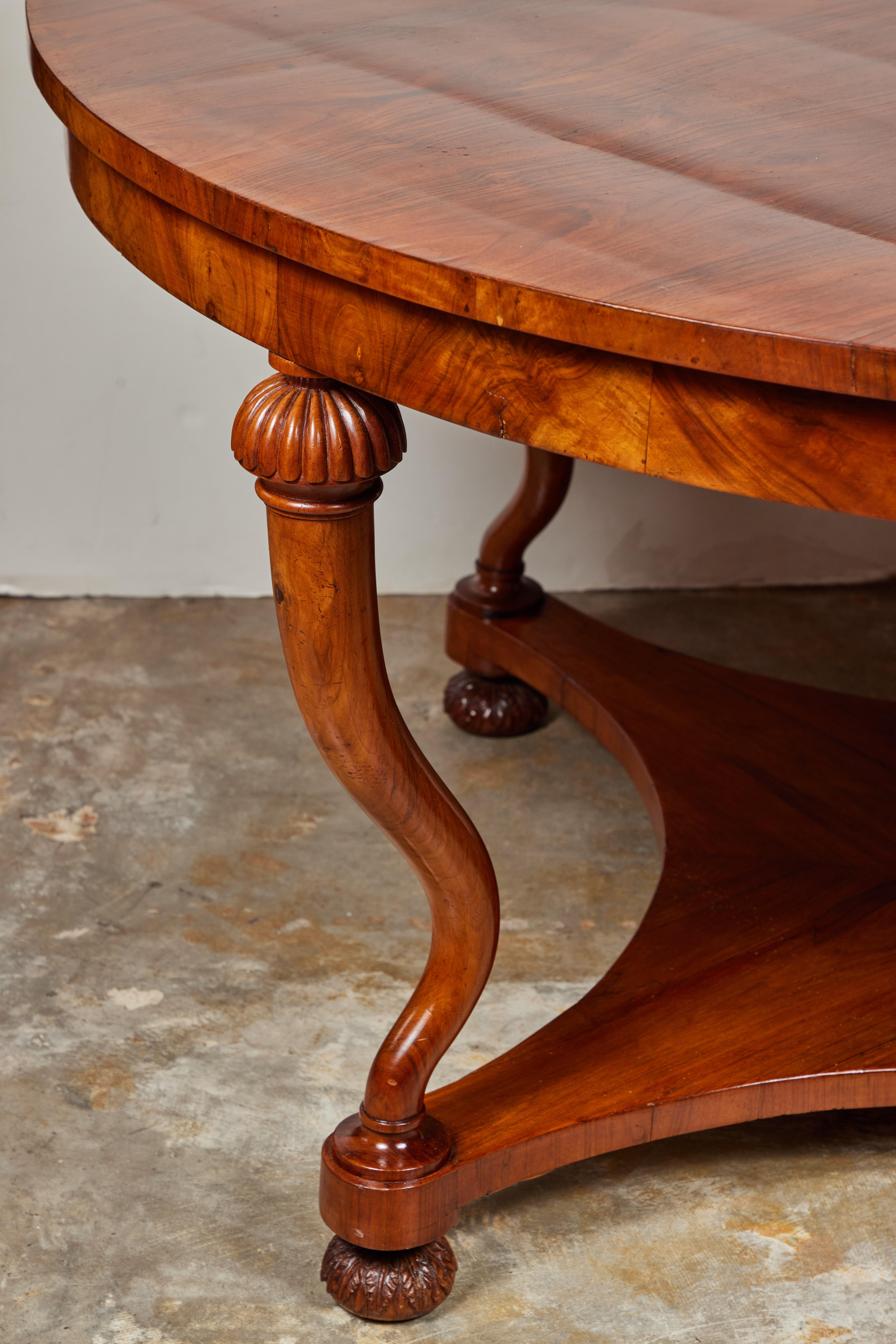 A beautiful, hand-carved, and book matched walnut, veneered center table on four serpentine legs above a scooped-edge base on foliate relief, bun feet.