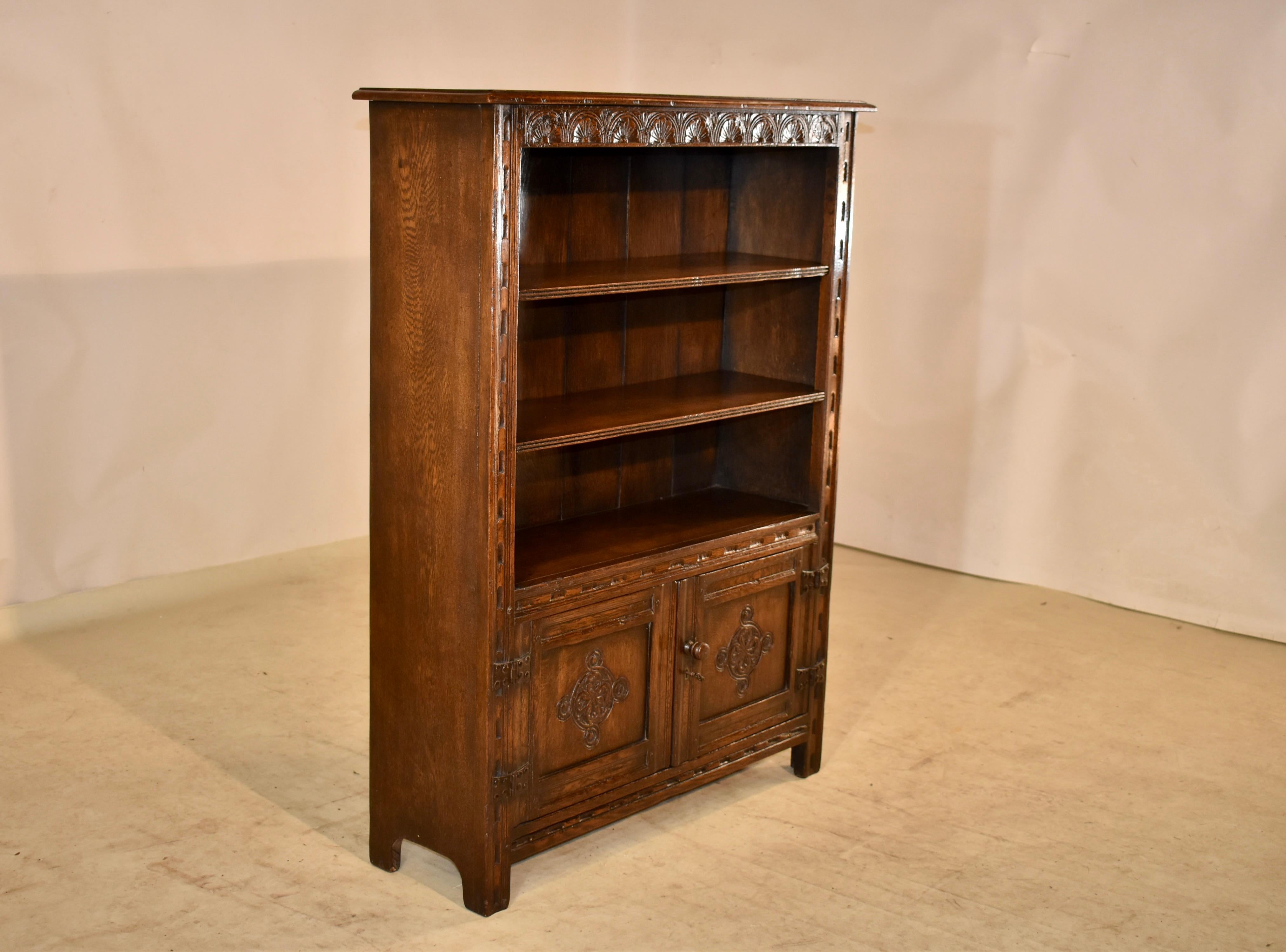Circa 1900 oak bookcase from England. The top has a beveled edge, following down to simple sides and hand carving on the front of the case and front of the shelves. There are three stationary shelves, overt lower doors, which open to reveal storage.