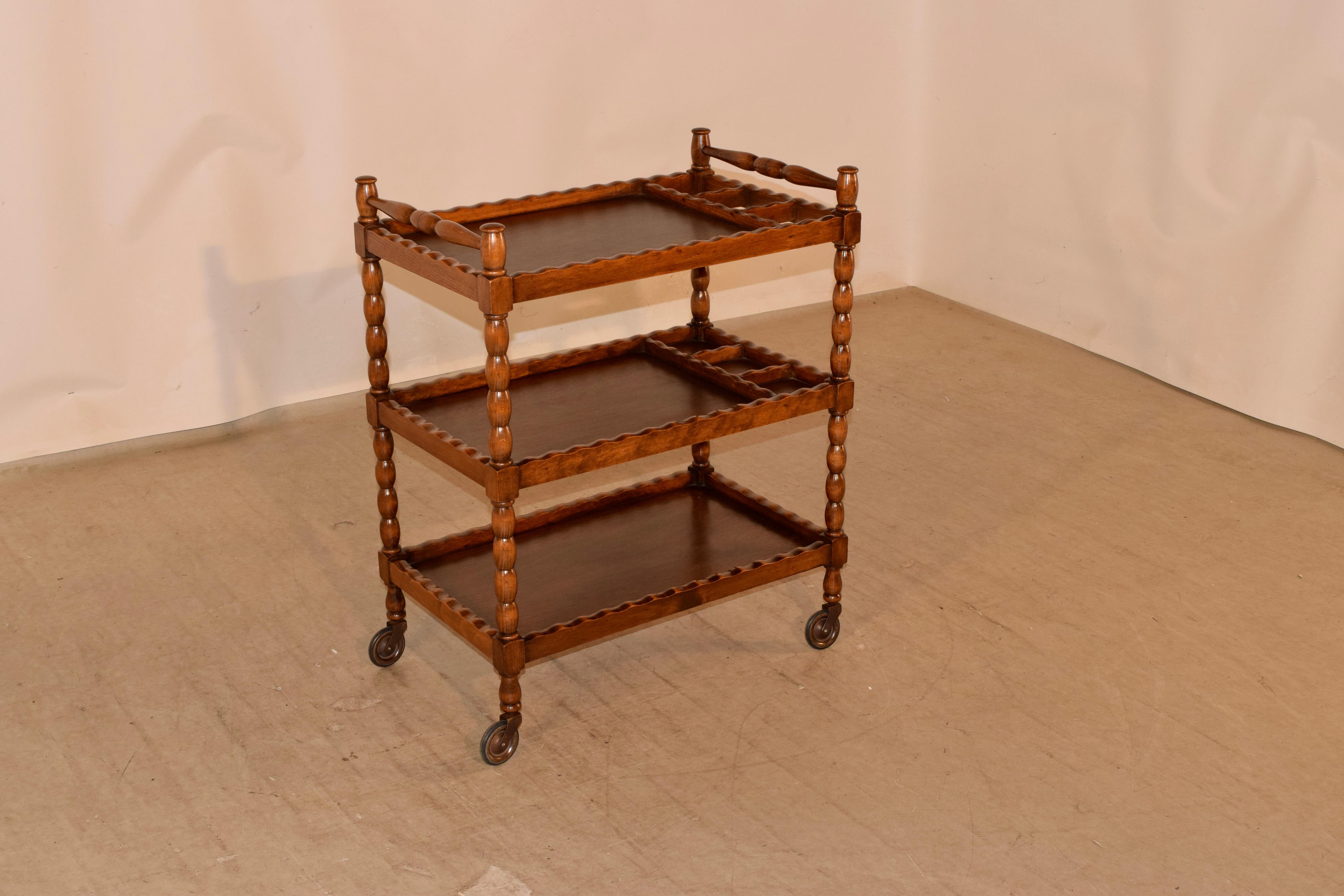 C. 1900 English oak drinks cart with turned handles over three shelves which have scalloped galleries and hand turned shelf supports and feet. The cart is supported on what appear to be the original casters.