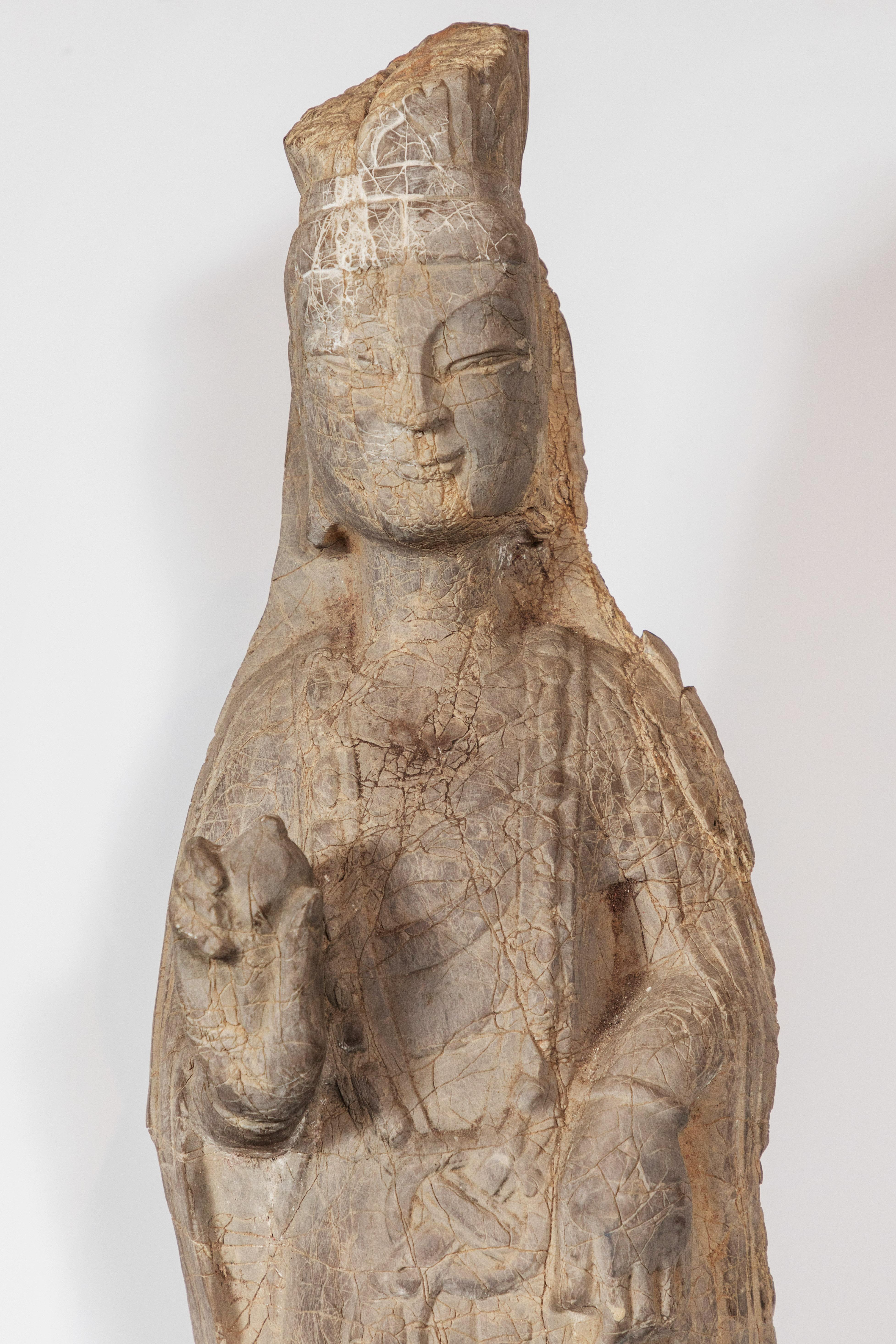 Elegant, carved stone figure of the goddess of compassion and mercy, Kwan Yin. She wears stylized robes and makes a gesture blessing. The surface is wonderfully worn and cracked throughout, giving it a far older appearance. Mounted on a custom, iron