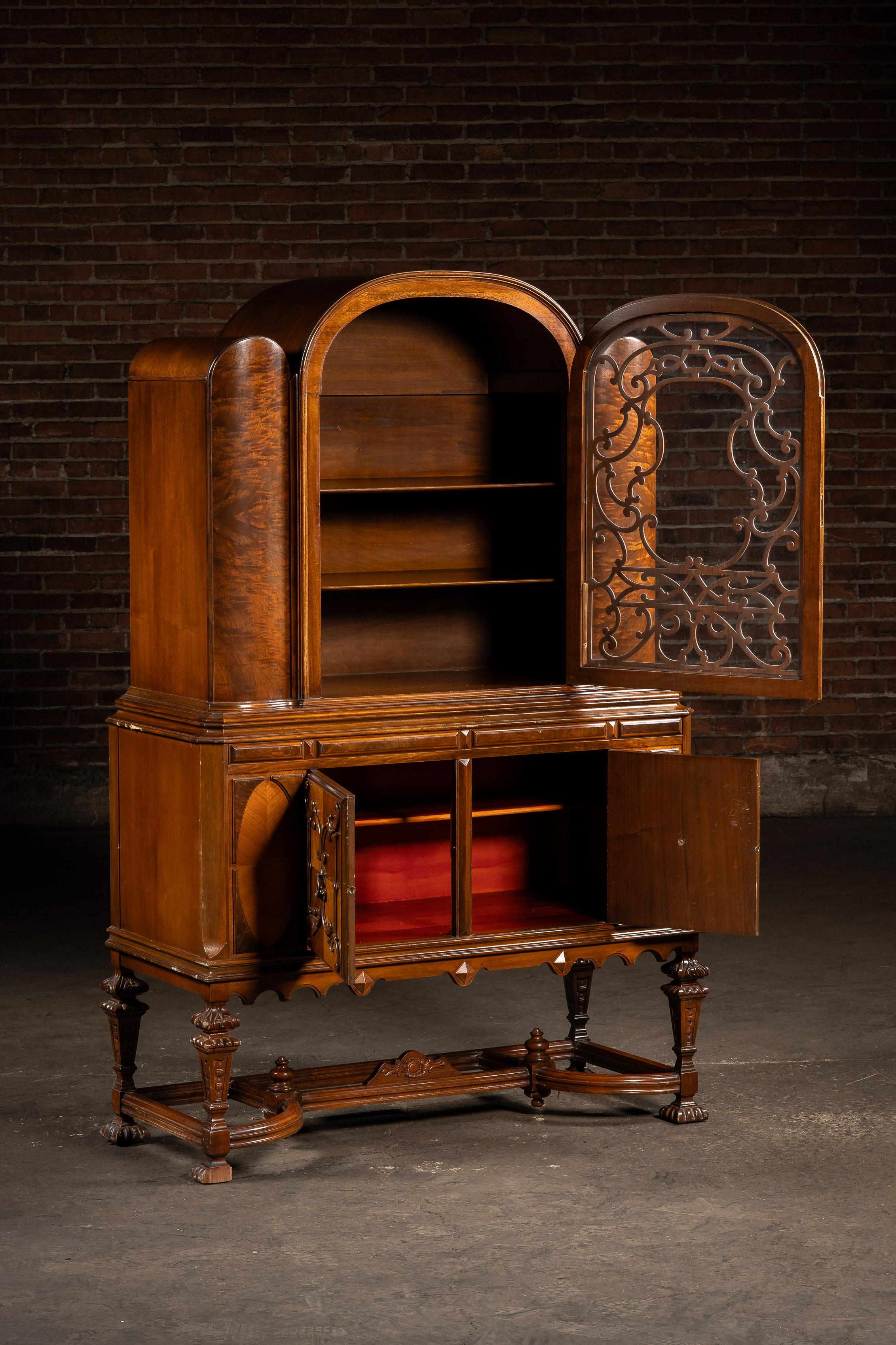 c. 1920s-1930s; (likely) Berkey & Gay Furniture Co. - Grand Rapids, MI

Tall display cabinet crafted in rich mahogany and walnut veneer, featuring an arched bonnet top and intricate carved fretwork overlaying a single glass door. The upper section