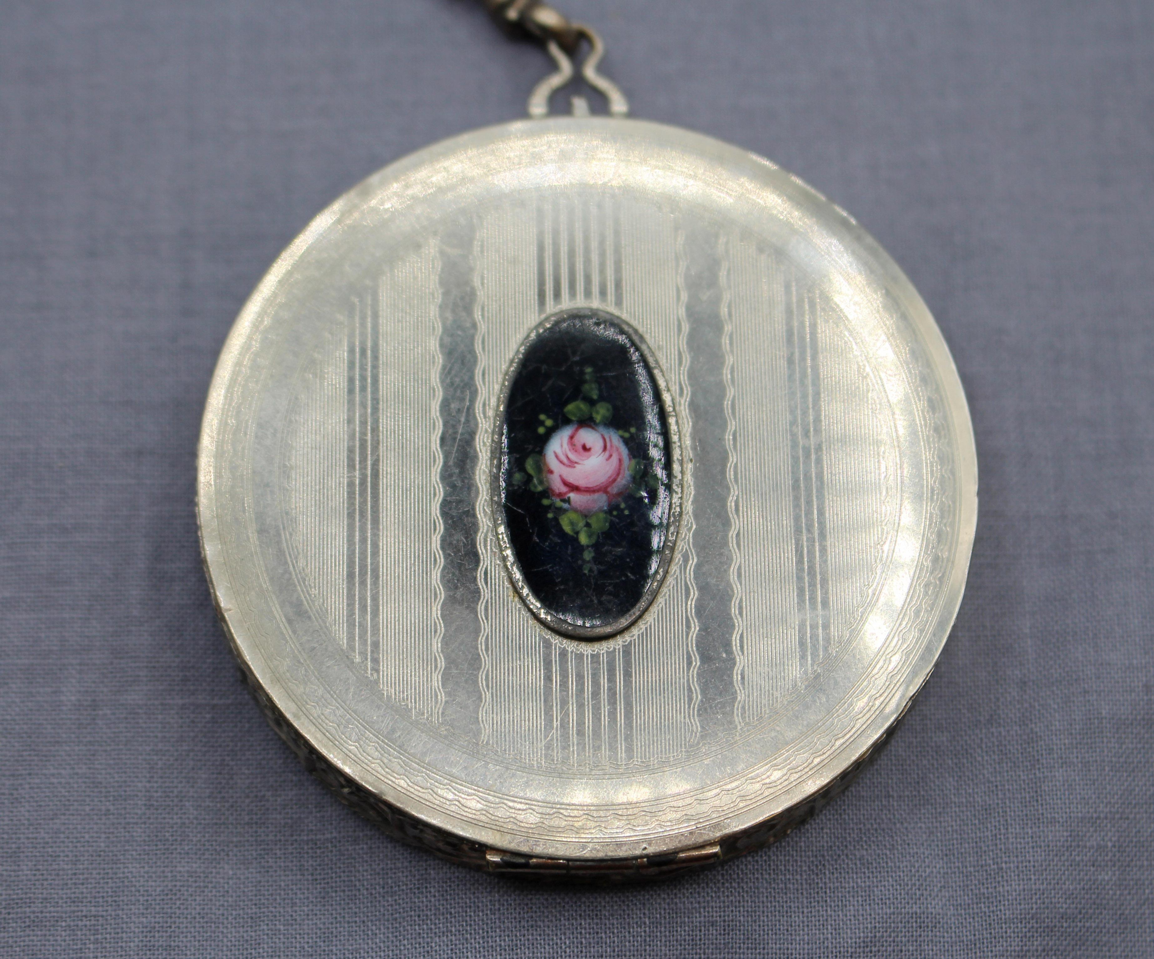Compacto Art Decó de mujer de los años 20-30 con placa de plata y cadena de muñeca. Inserto con placa oval negra pintada a mano con una rosa. Efecto crepitante en el panel negro. Puff, espejo y polvos en el interior. La decoración mecanizada es