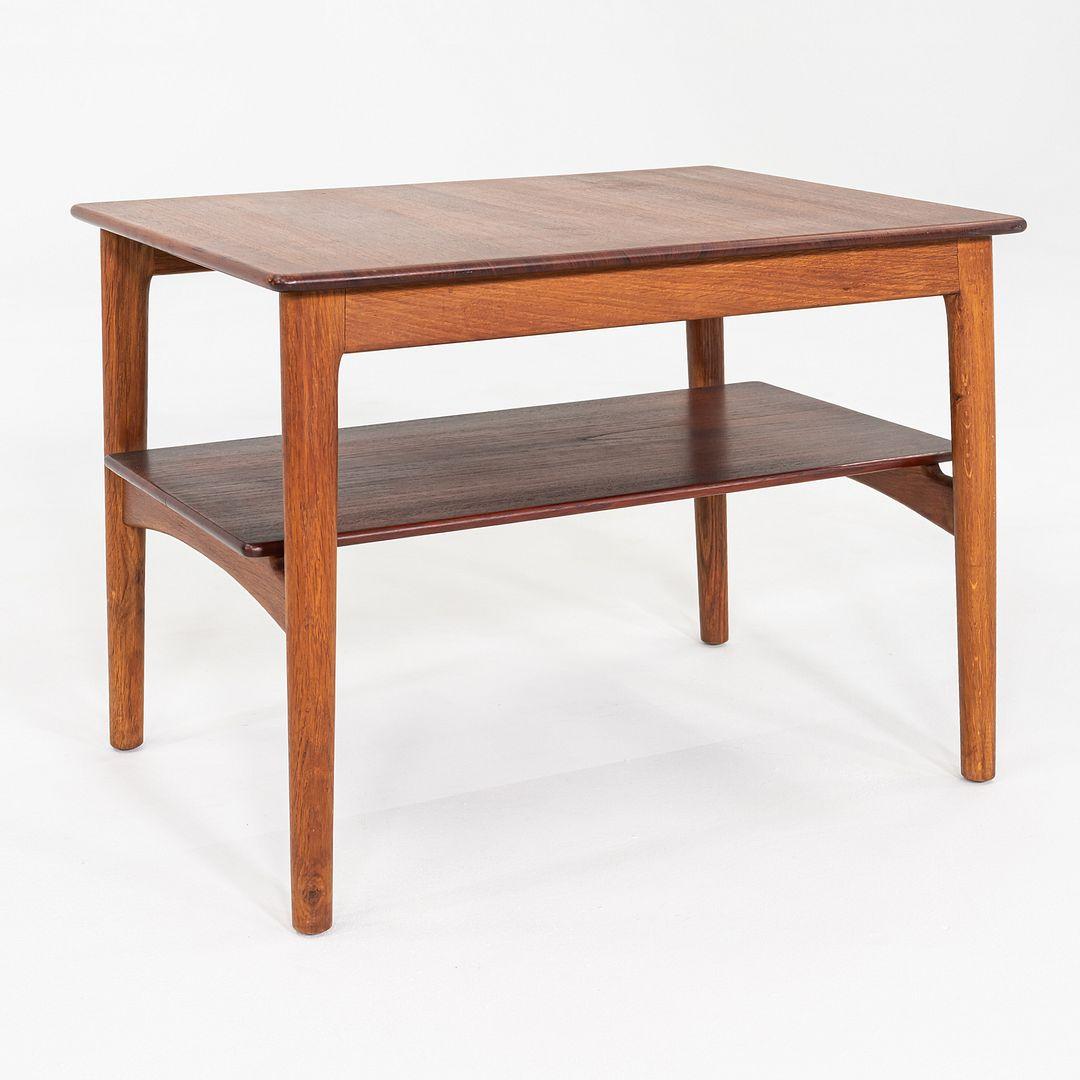 This is a Rectangular Side or End Table, designed by Hans Wegner and produced by Johannes Hansen in Denmark. It features a two-tiered design, having a teak top and bottom shelf, accompanied by contrasting oak legs. The table's shape and size make it