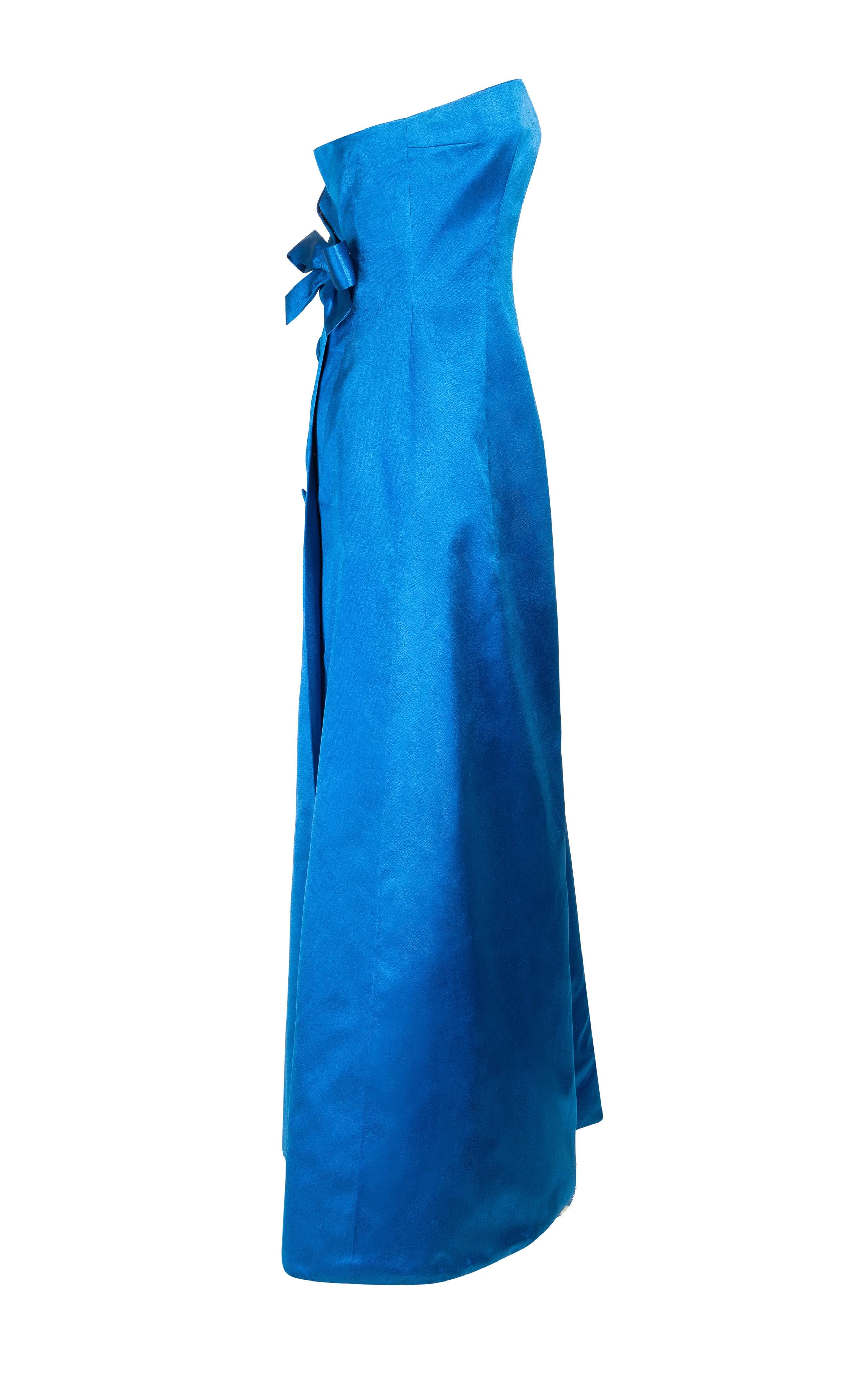 c. 1959 Jean Patou by Karl Lagerfeld Couture trägerloses Abendkleid aus blauem Satin. Dazu passende übergroße Stoffknöpfe und große Schleife am Rücken. Subtiler Wickeleffekt am Rücken mit seitlichem Überschlag am Rücken. Eingebautes Korsett aus