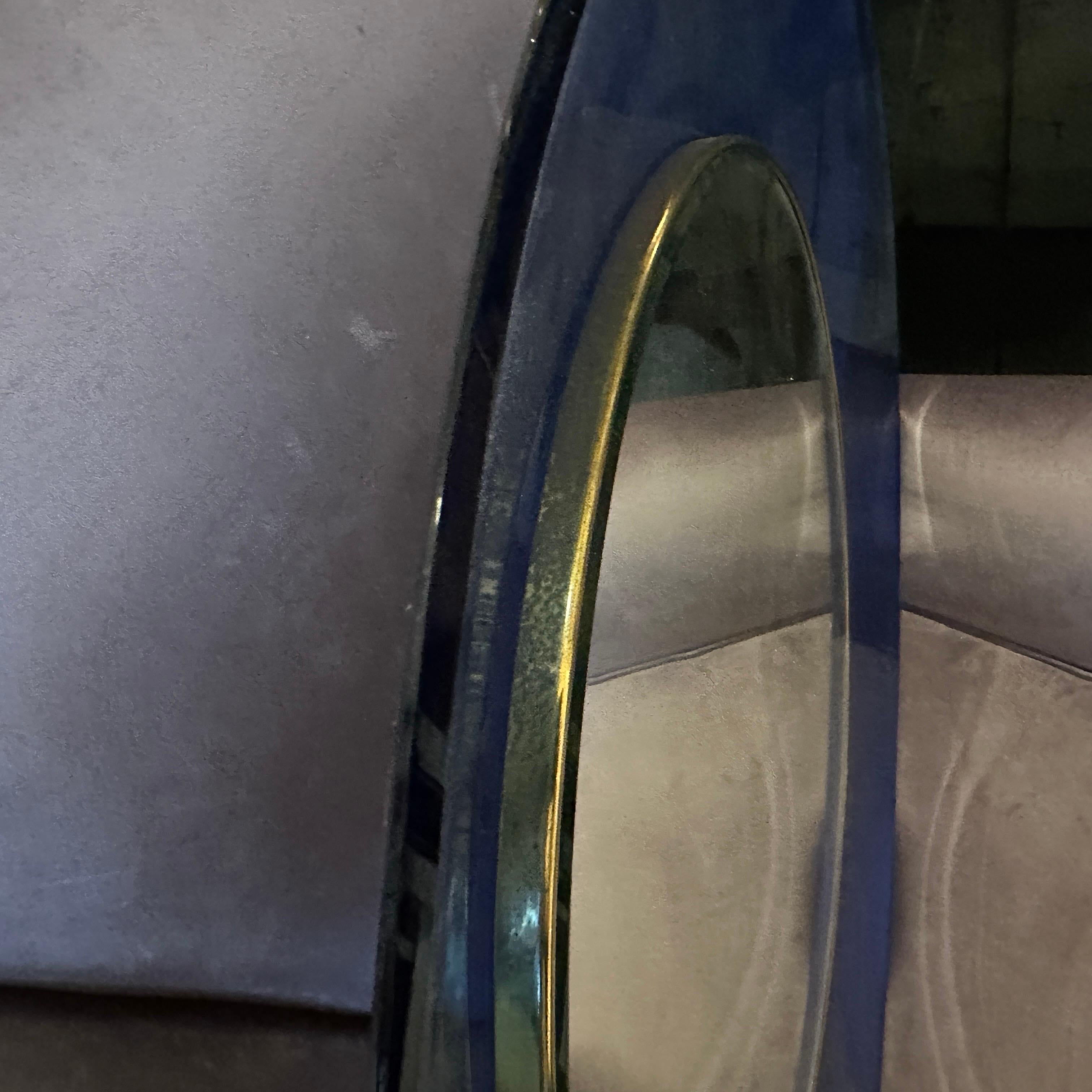 The C. 1960 Mid-Century Modern Blue Glass and Brass Round Wall Mirror, Mod. 1669, designed by Max Ingrand for Fontana Arte, is an iconic example of Italian mid-century design. Max Ingrand, a celebrated glass artist and designer, was known for his