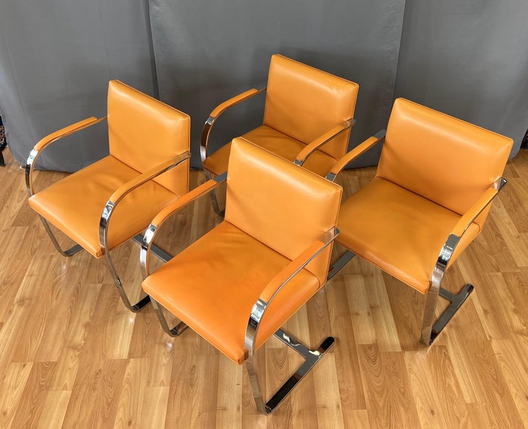 Here is a wonderful circa 1970s set of four flat bar Brno armchairs in Orange leather, designed by Mies Van der Rohe. 
Made by Gordon International, in the country of Argentina. Label of maker is under the seat, with country under a flat bar.
