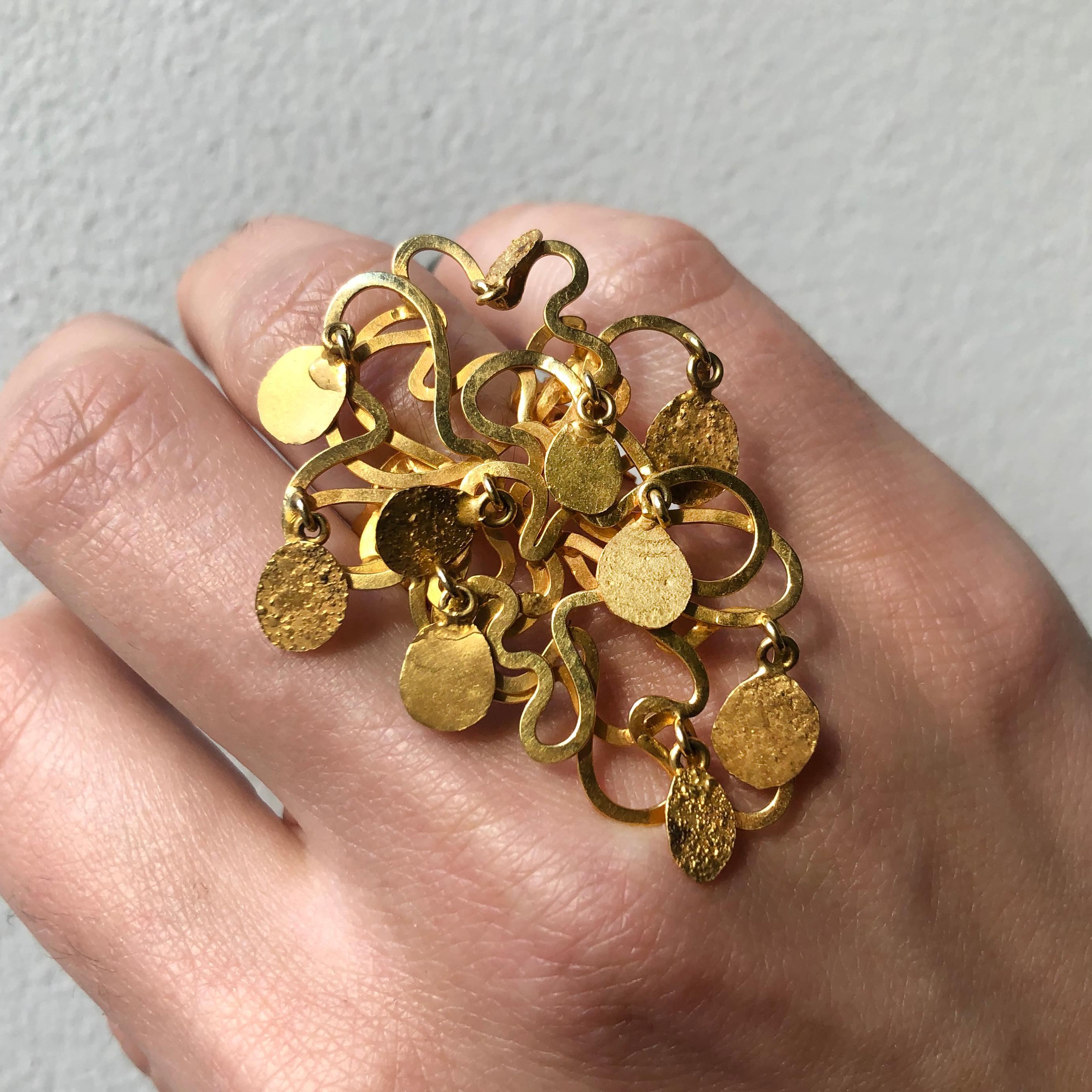 A gold ring with articulated ornaments, by sculptor E.R. Nele, c. 1990. Ring size 7. E. R. Nele (b. 1932) is a German artist known primarily for large-scale metal sculptures. She studied in Berlin and at the Central School of Arts and Crafts,