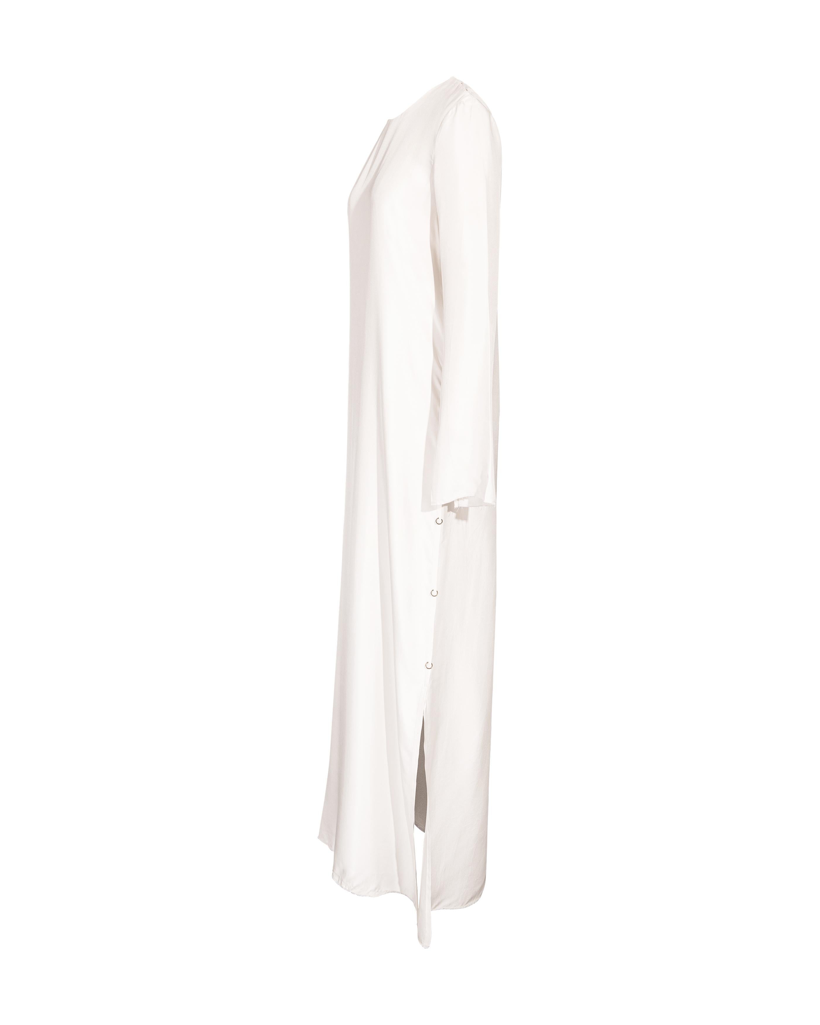 Robe à manches longues en soie blanche S/S 2016 Calvin Klein à manches ouvertes et détails de boucles en bronze sur les côtés, avec ourlet brut non fini. Fermeture par boutons-pression aux épaules. Contenu du tissu : 100% soie. En très bon état