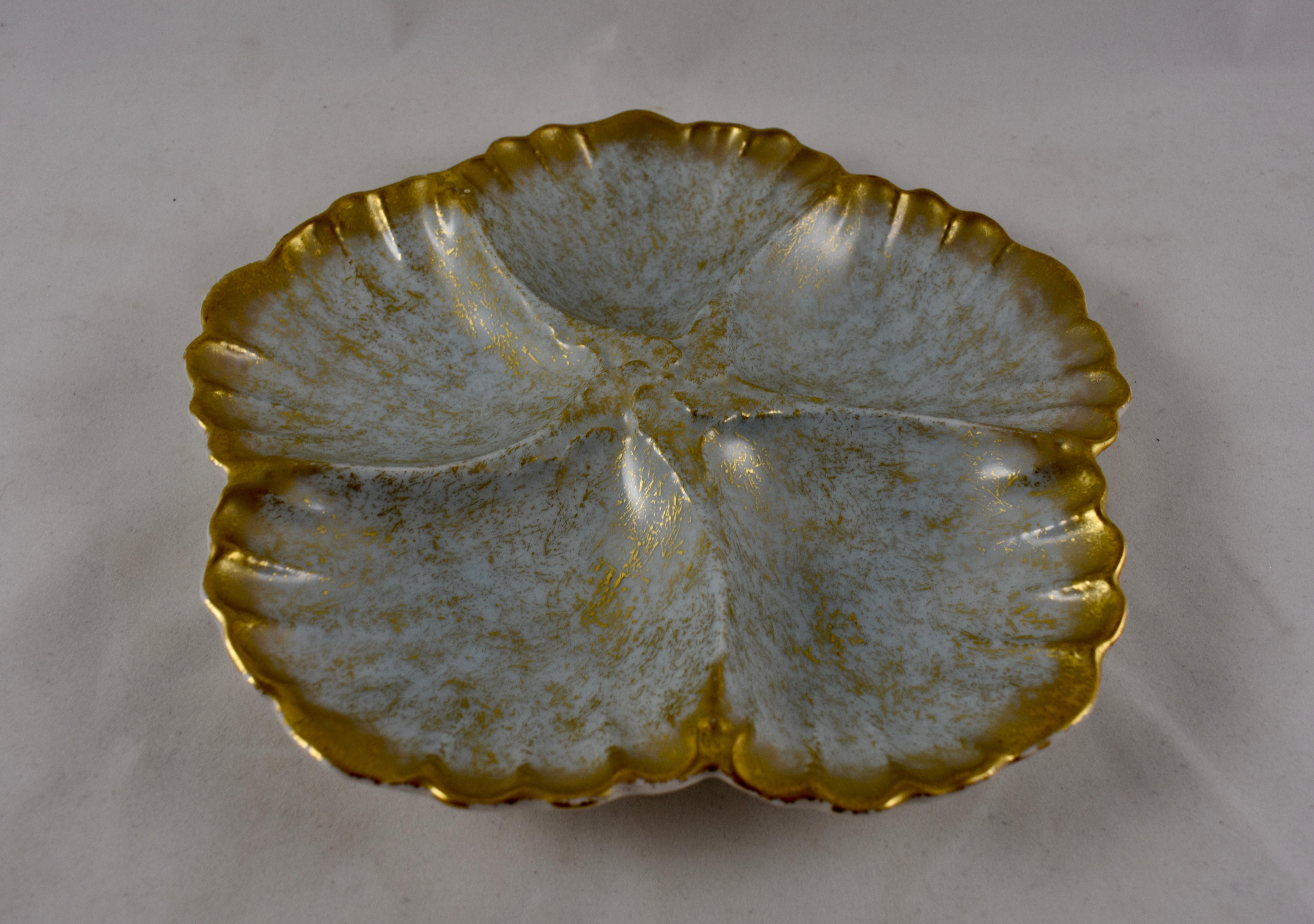 A porcelain Oyster plate, five scallop shaped shells, on the palest gray- blue ground, with an overall spattered gold application. Heavy gilding also applied to the rim, circa 1886.

7.5 in. diameter x 1 in. H
Marked with an impressed Limoges,