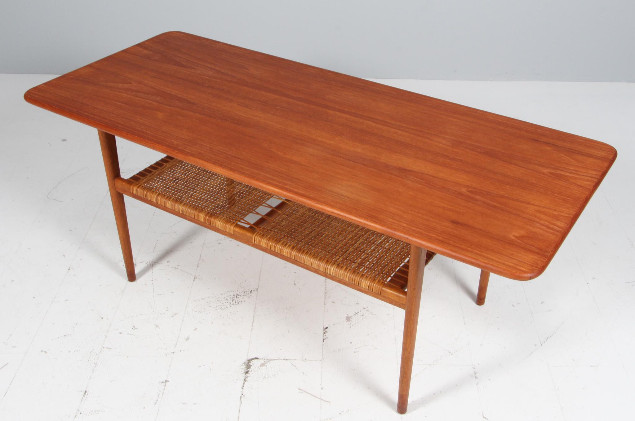 C. B. Hansen coffee table with top and shoes of teak. Legs of oak. Newspaper shelf in cane.

Made in Denmark in the 1960s