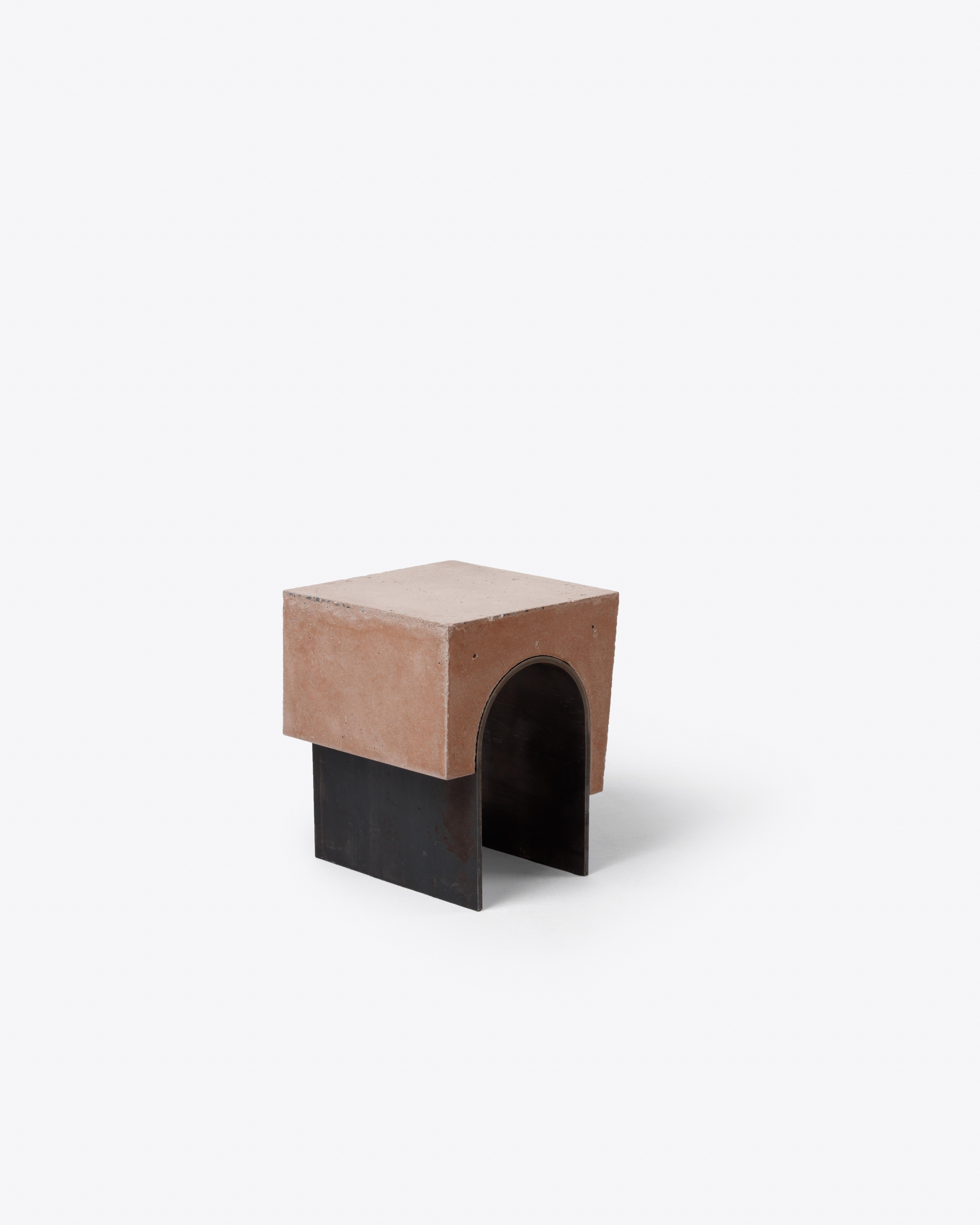 This compact stool pairs a rosé-tinted concrete block with a hollow arched base in oxidized steel. Its simple geometry
carries architectural cues—the arch as support, the offset tension between weight and void. Both sculptural and
utilitarian, it