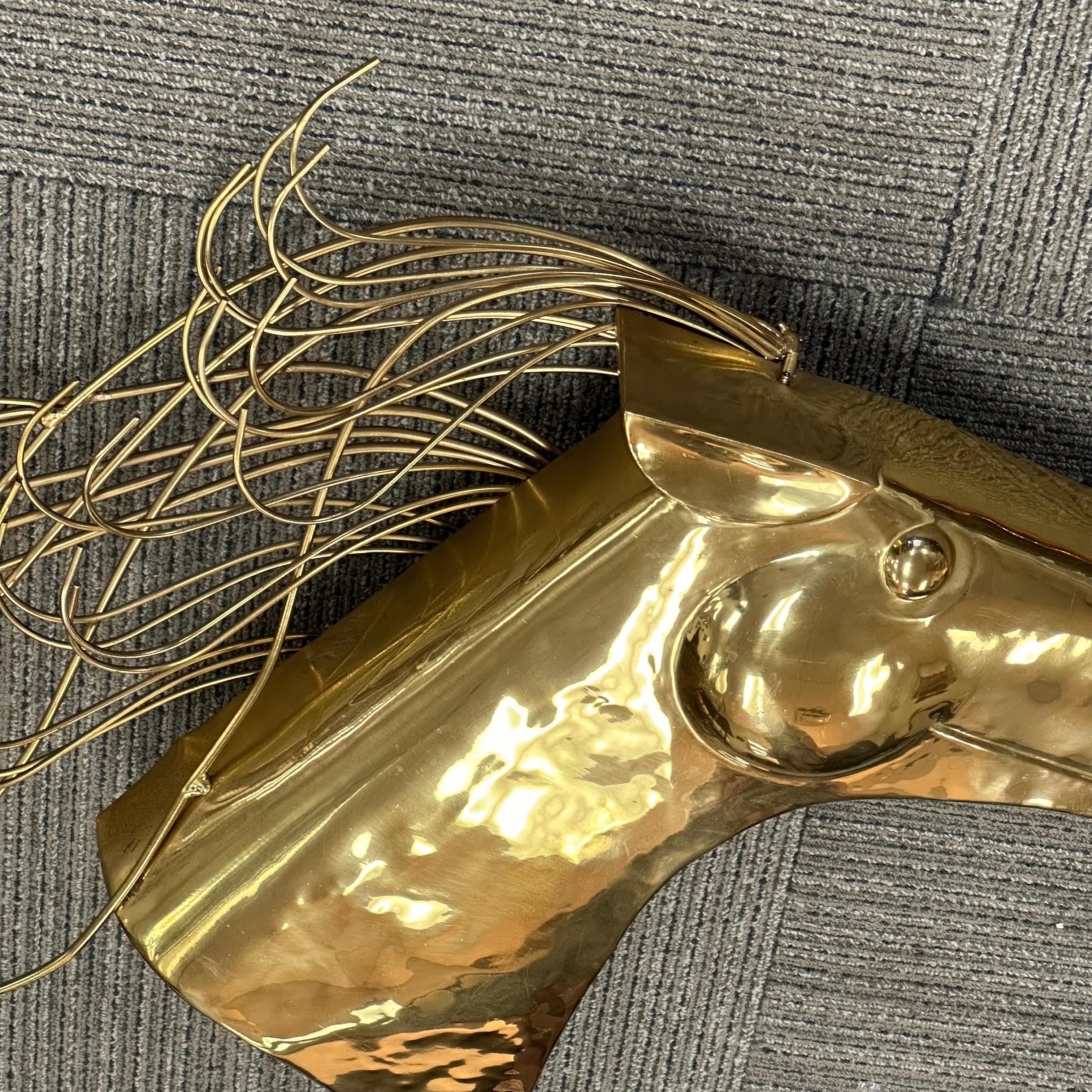A beautiful polished brass wall sculpture of a stylized horse head with a flowing mane. The head of the horse is polished brass. The mane is composed of individual brass rods. The piece is signed 