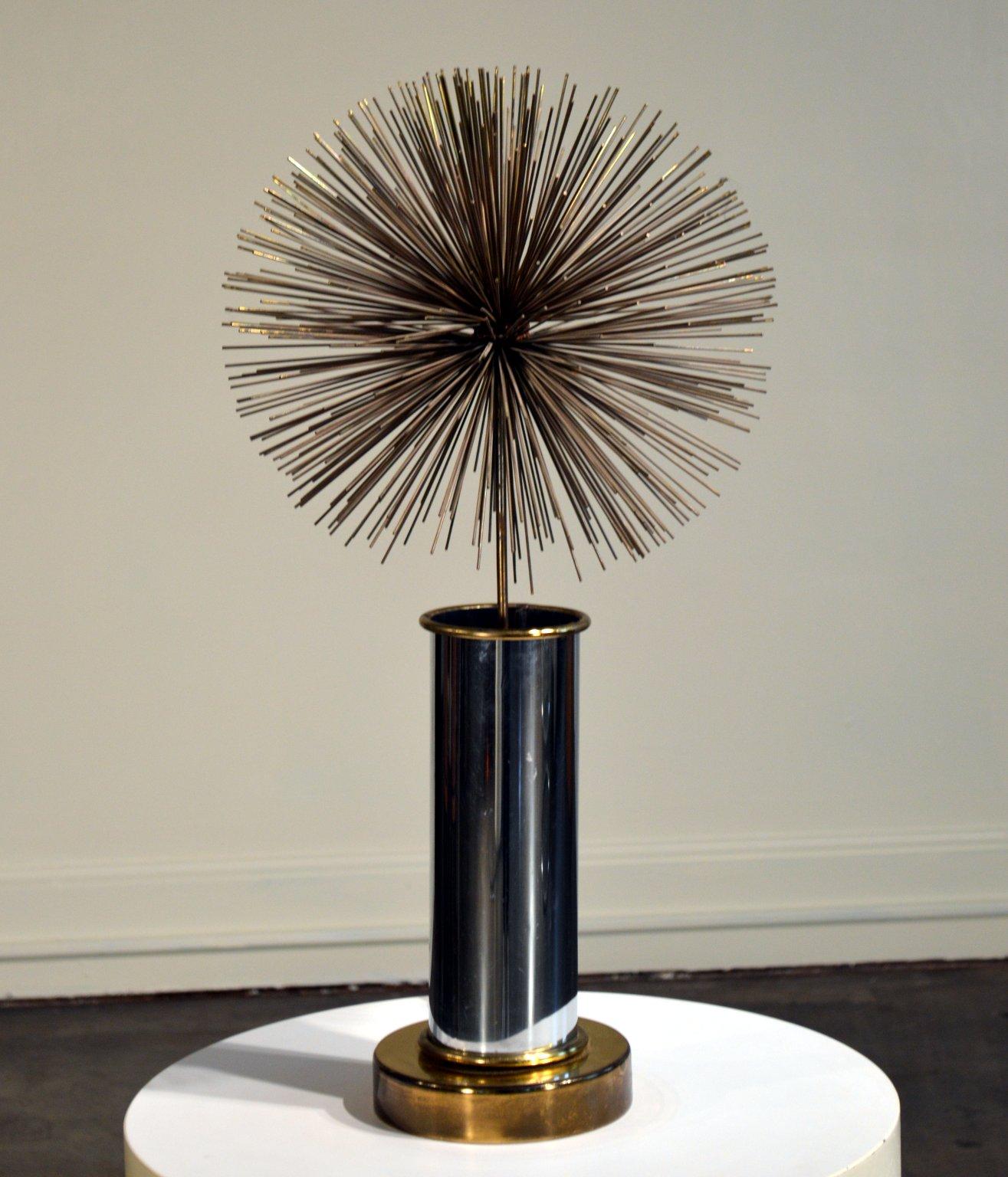 Mixed metal lighted pom-pom sculpture by C. Jere.

A sturdy cylindrical chrome and brass base holds the light socket and hand formed brass and steel pom-pom sculpture. This lamp casts a gentle uplight; used as a night-light it throws subtle to