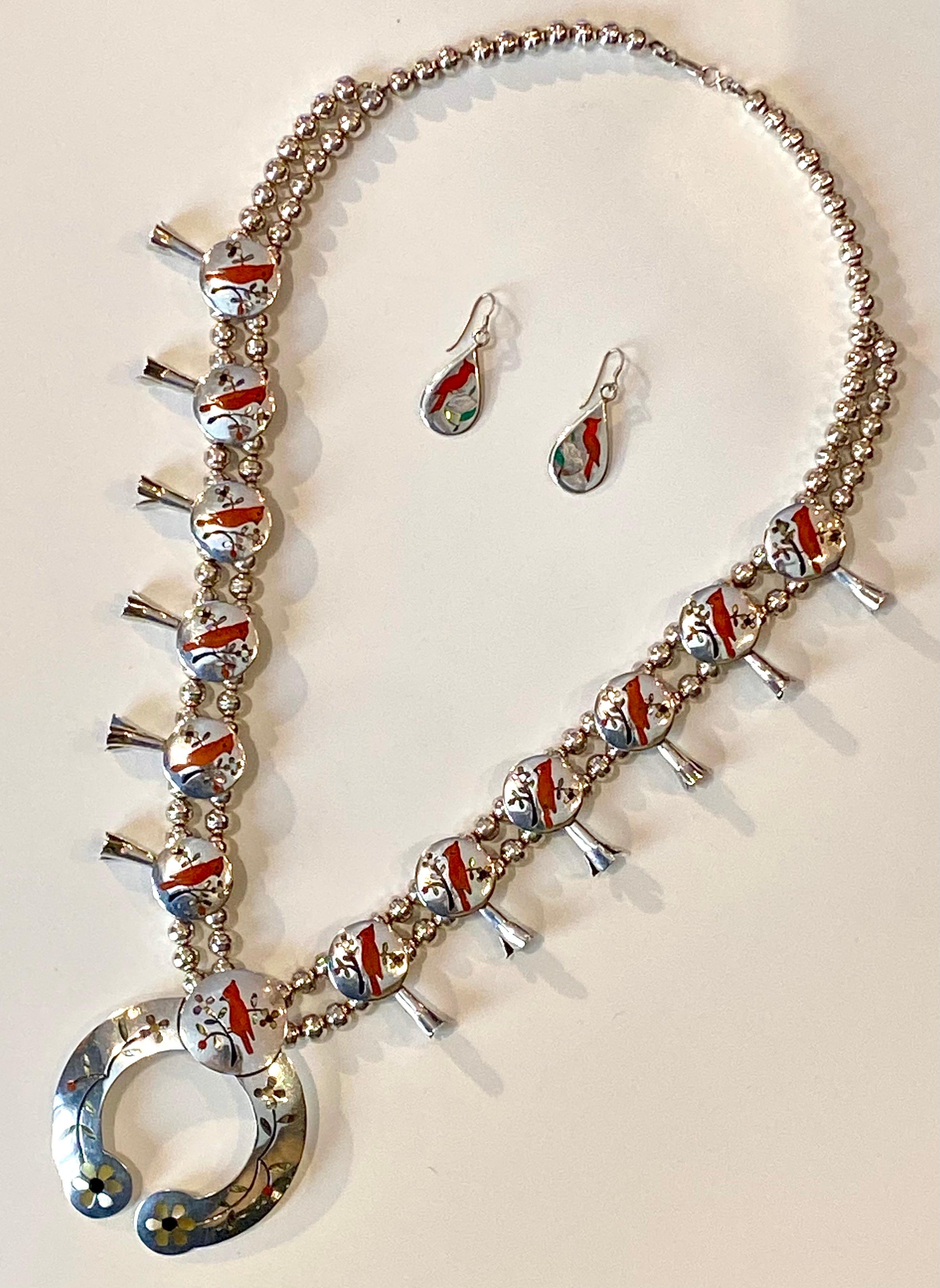 A beautiful bench made Navajo squash blossom necklace by C. M. Yazzie. Hand crafted in sterling silver with inlaid natural red coral, abalone mother of pearl and black jet. It features the image of a red cardinal sitting on a branch on each of the