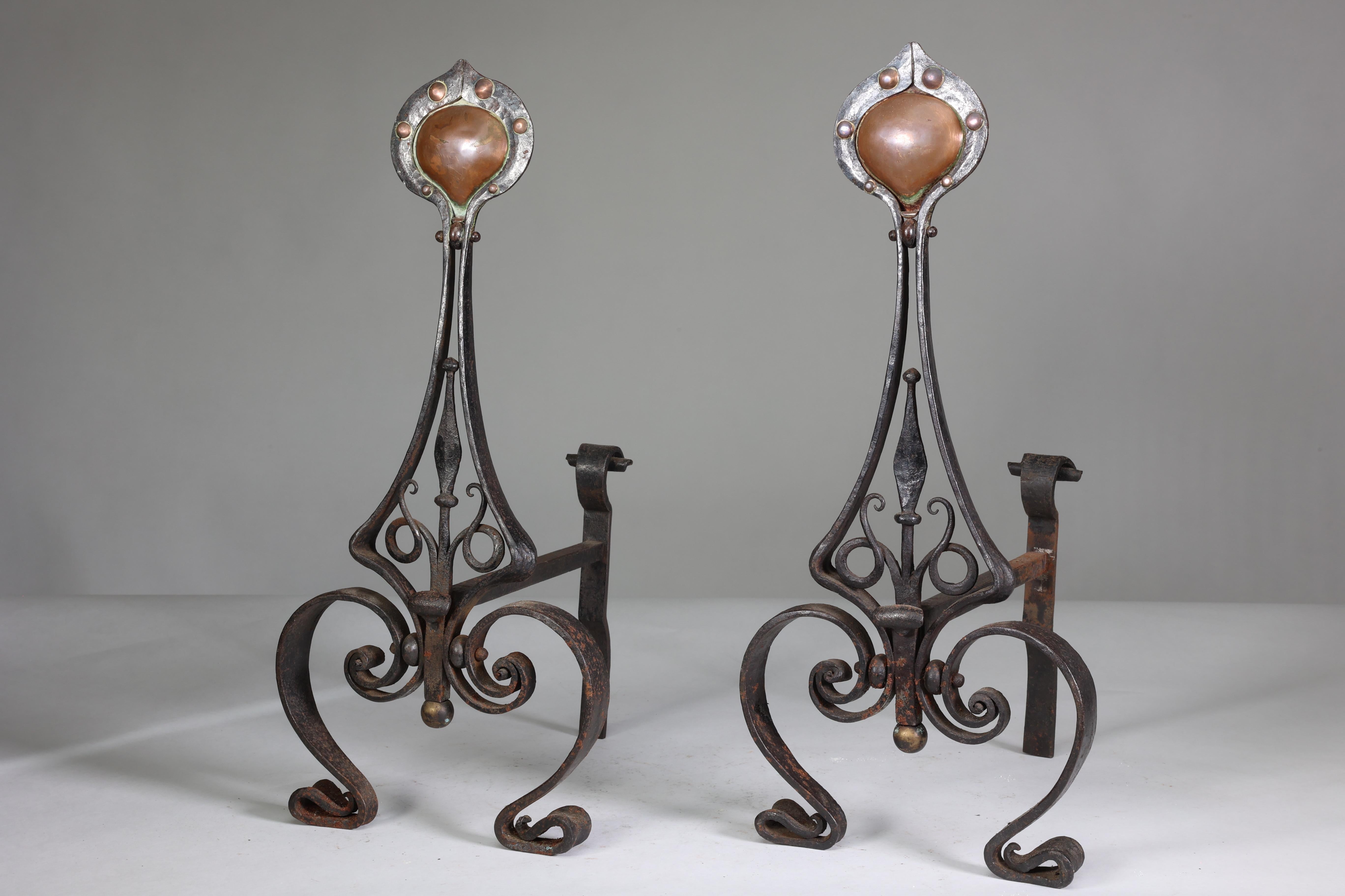 C R Ashbee for The Guild of Handicraft, attributed. An early pair of hand-wrought iron fire dogs with inset copper hearts to the tops. Very fine blacksmiths work with hand-hammered flat flowerheads flowing down to frame the central spearhead and