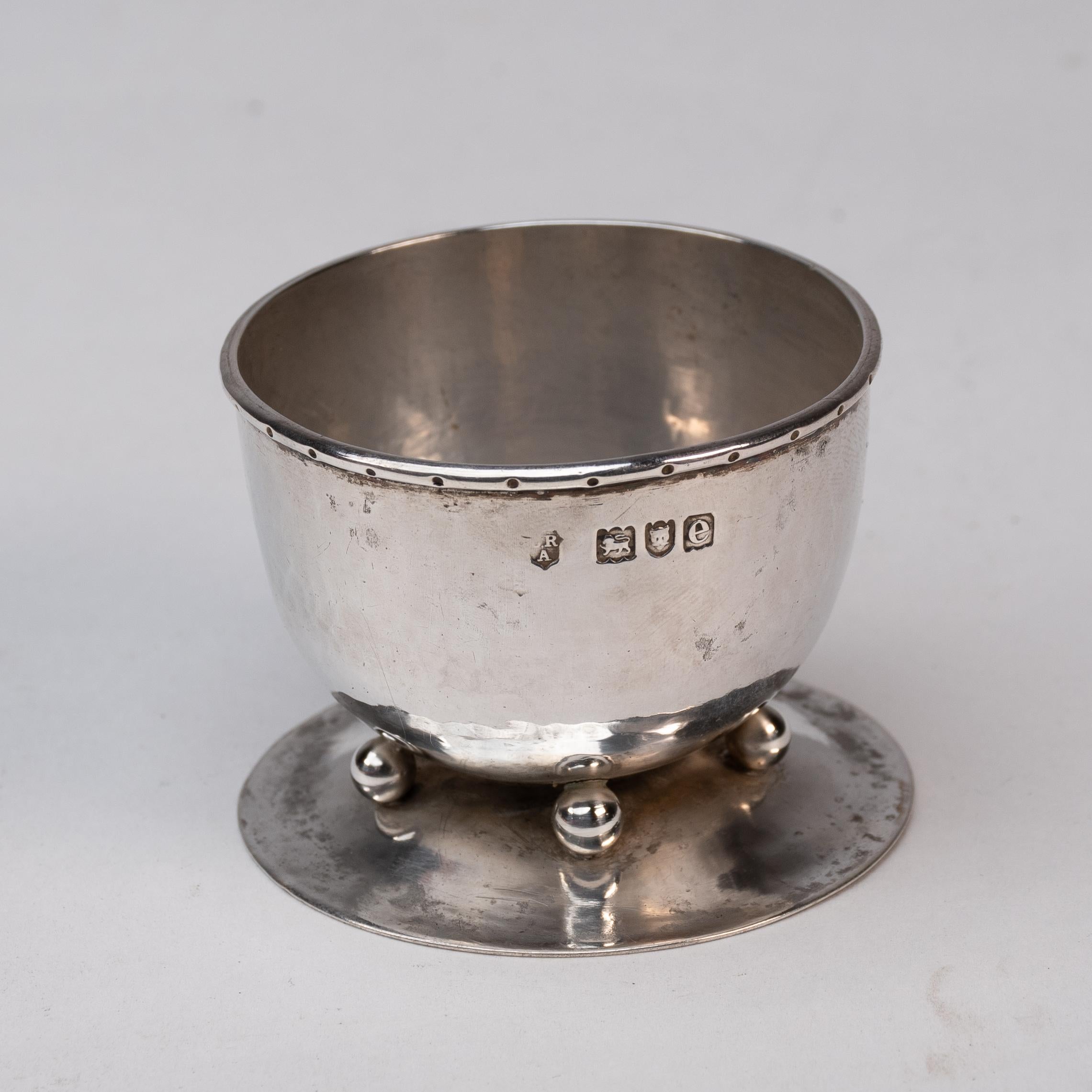 C. R. Ashbee per la Guild of Handicraft.
Una rara coppia di saliere in argento Decorative Crafts con bordi arrotolati e decorazioni a puntini sui bordi della ciotola, poggiate su quattro piedini a sfera su una base svasata.
Ashbee ritornò a questo