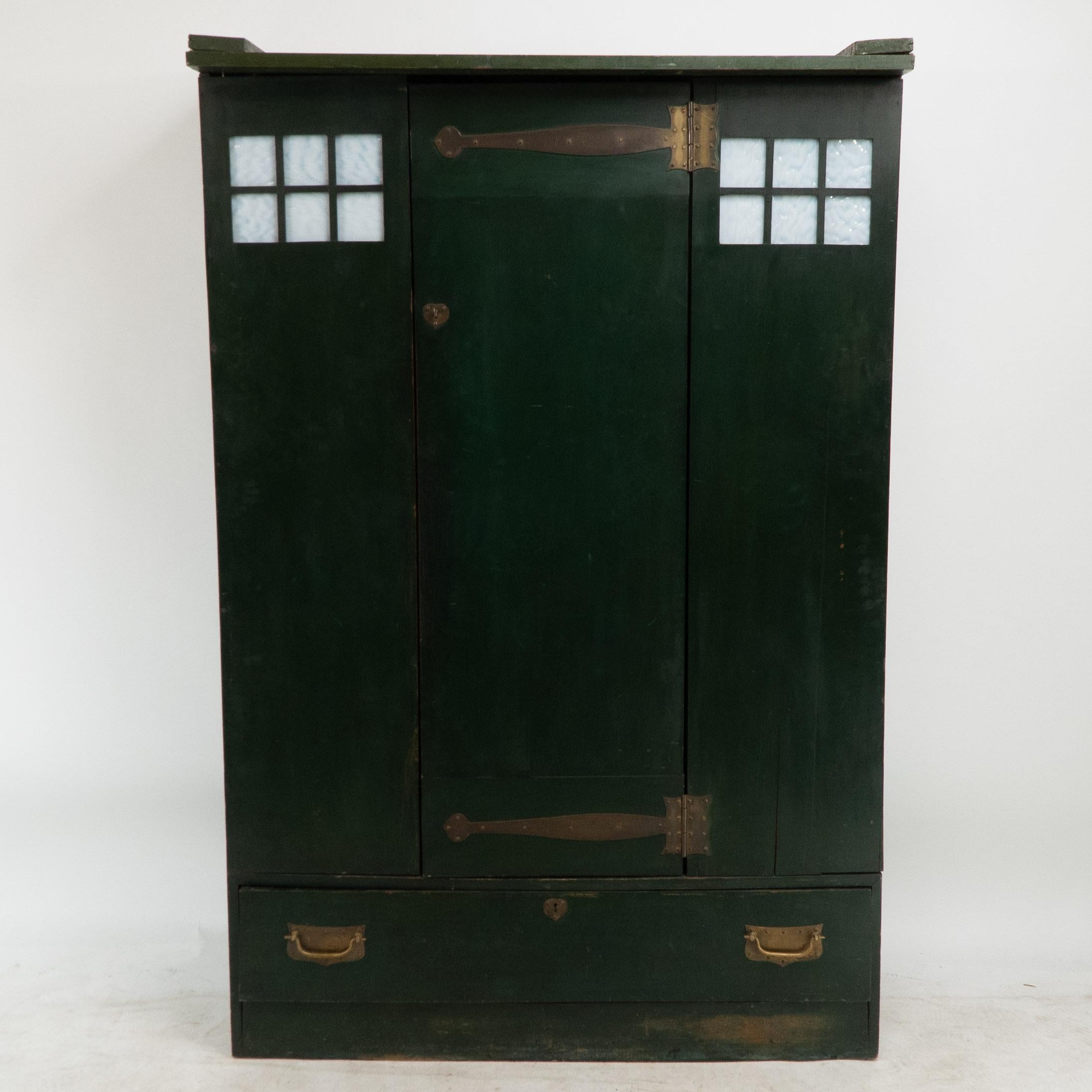 Charles Rennie Mackintosh (1868-1928), made by Guthrie and Wells. 
A Glasgow School Arts and Crafts stained green cypress wood wardrobe, with white opaque textured square glass details to the top. The central door and a large lower drawer with brass