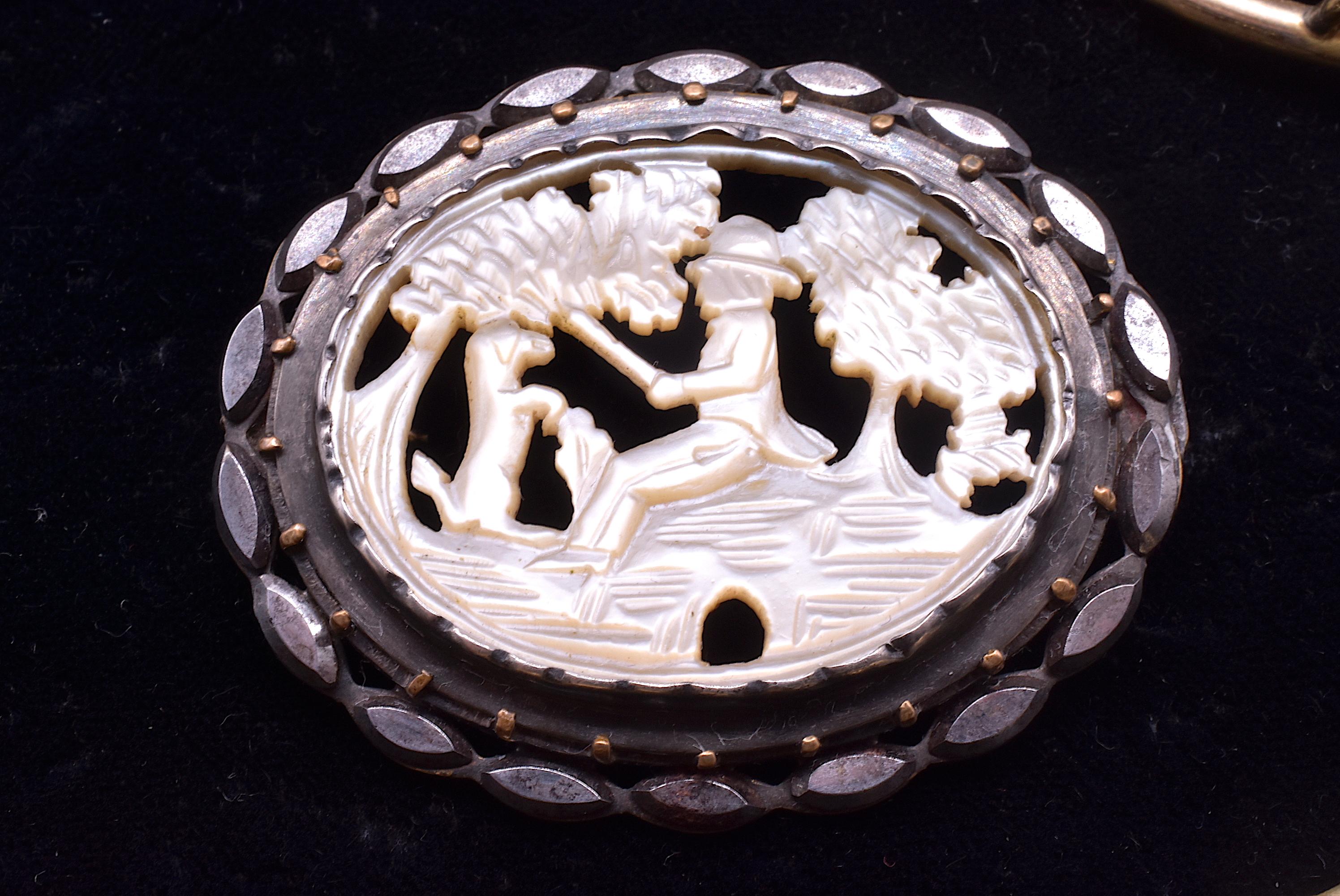 Enchanting brooch of cut steel and mother of pearl with carved image of a faithful dog standing at attention as his human companion peacefully angles for a catch under the shade of a tree. The scene is carved from Mother of Pearl and mounted in cut
