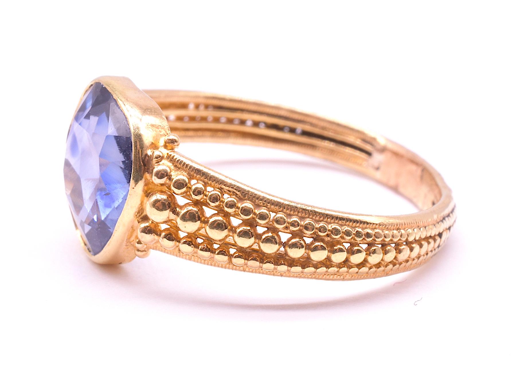 Our 18K open backed sapphire ring has unusual hand crafted gold bead work  in concentric rows all along the band evoking similarity to cannetille work. The sapphire is a lovely translucent cornflower blue. The gold beads are set in graduated sizes,