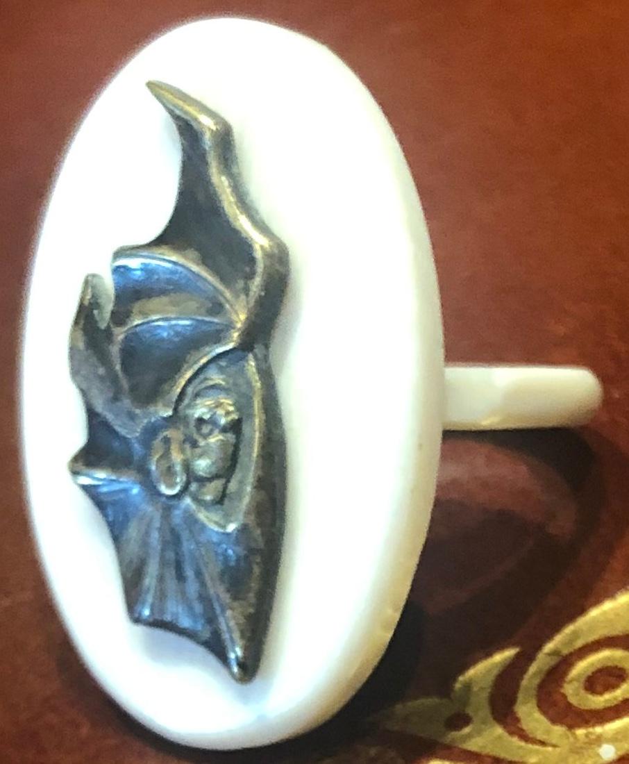Nuestro anillo Shakudo representa un murciélago montado sobre un anillo de hueso. El oficio de Shakudo se originó en Japón durante el periodo Samurai.  Artistas de talento fabricaban ornamentos para adornar armas y armamento.  Cuando terminó el