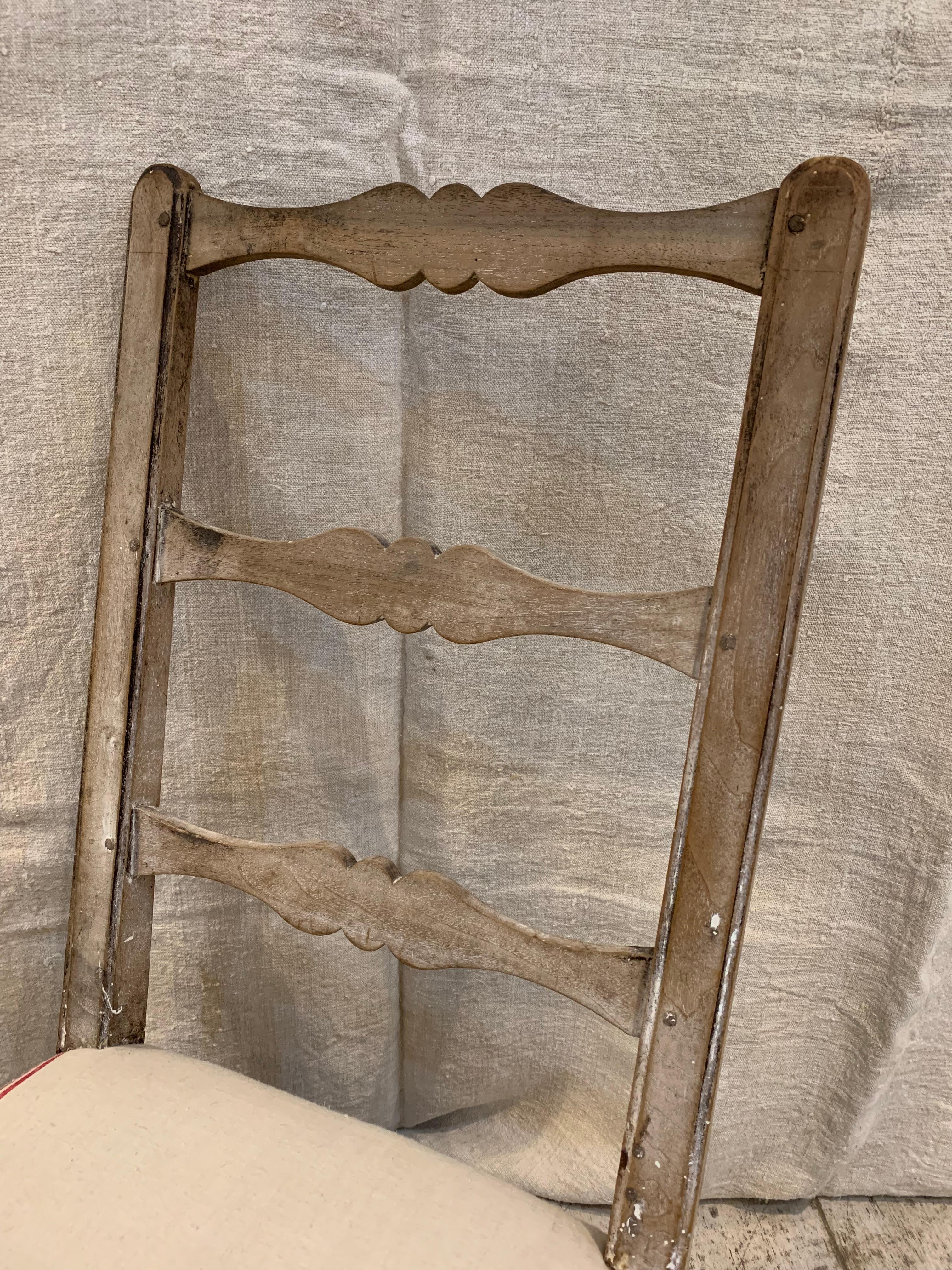 A charming C18th provincial french oak chair which has a tall ladder back, turned legs and curved stretcher.
The low but comfortable seat has been upholstered in a vintage off white french fabric with red stripes to the sides-there are a few marks