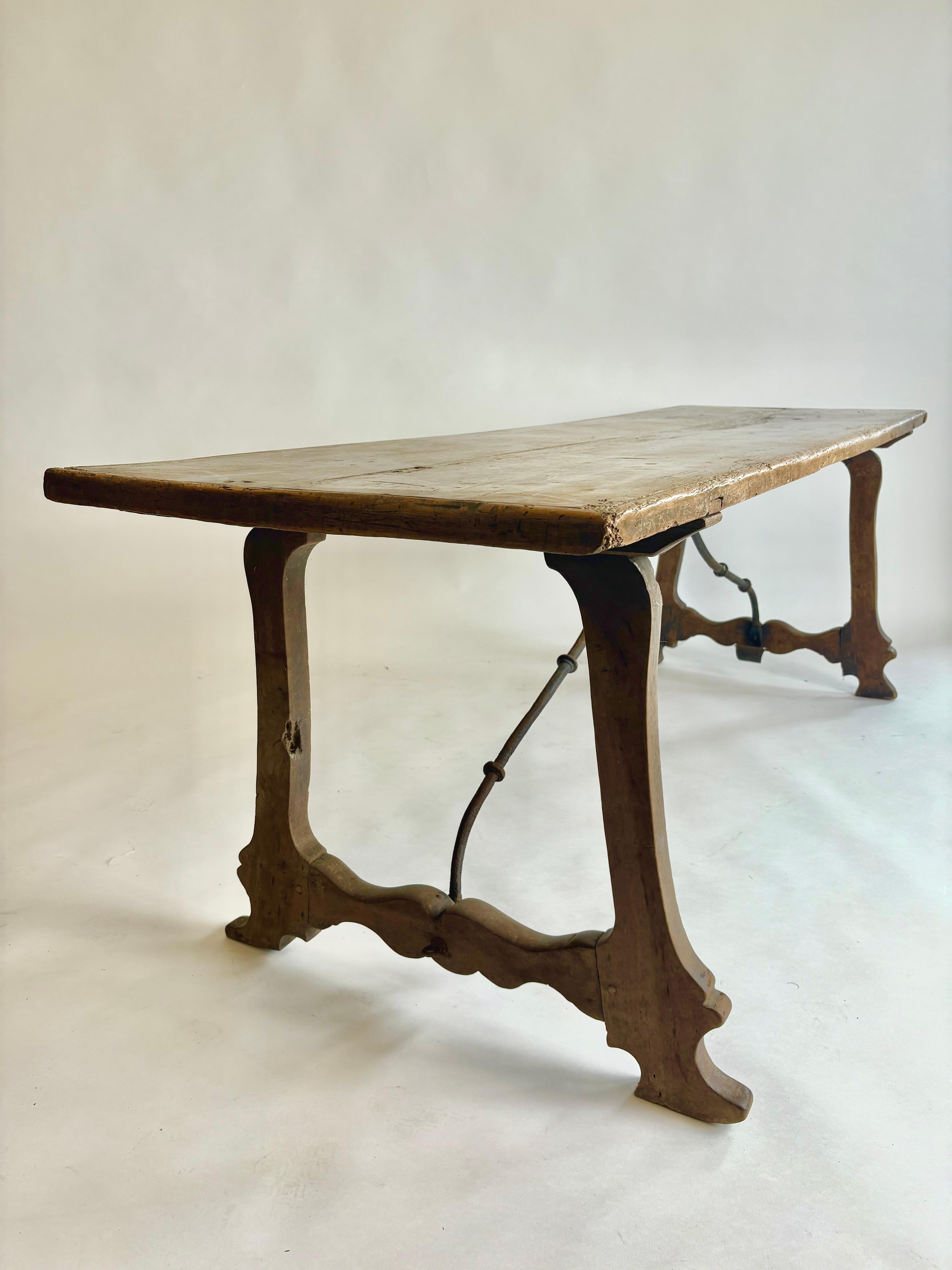 Eine wunderbare C18 th Spanisch Nussbaum langen Tisch mit einem 2-Planken-Platte mit  hochgezogene Stollenenden  auf  2 endständige Silhouetten-Stützen im naiven, primitiven Landhausstil, verbunden durch die originalen eisengeformten Bahren. Alles