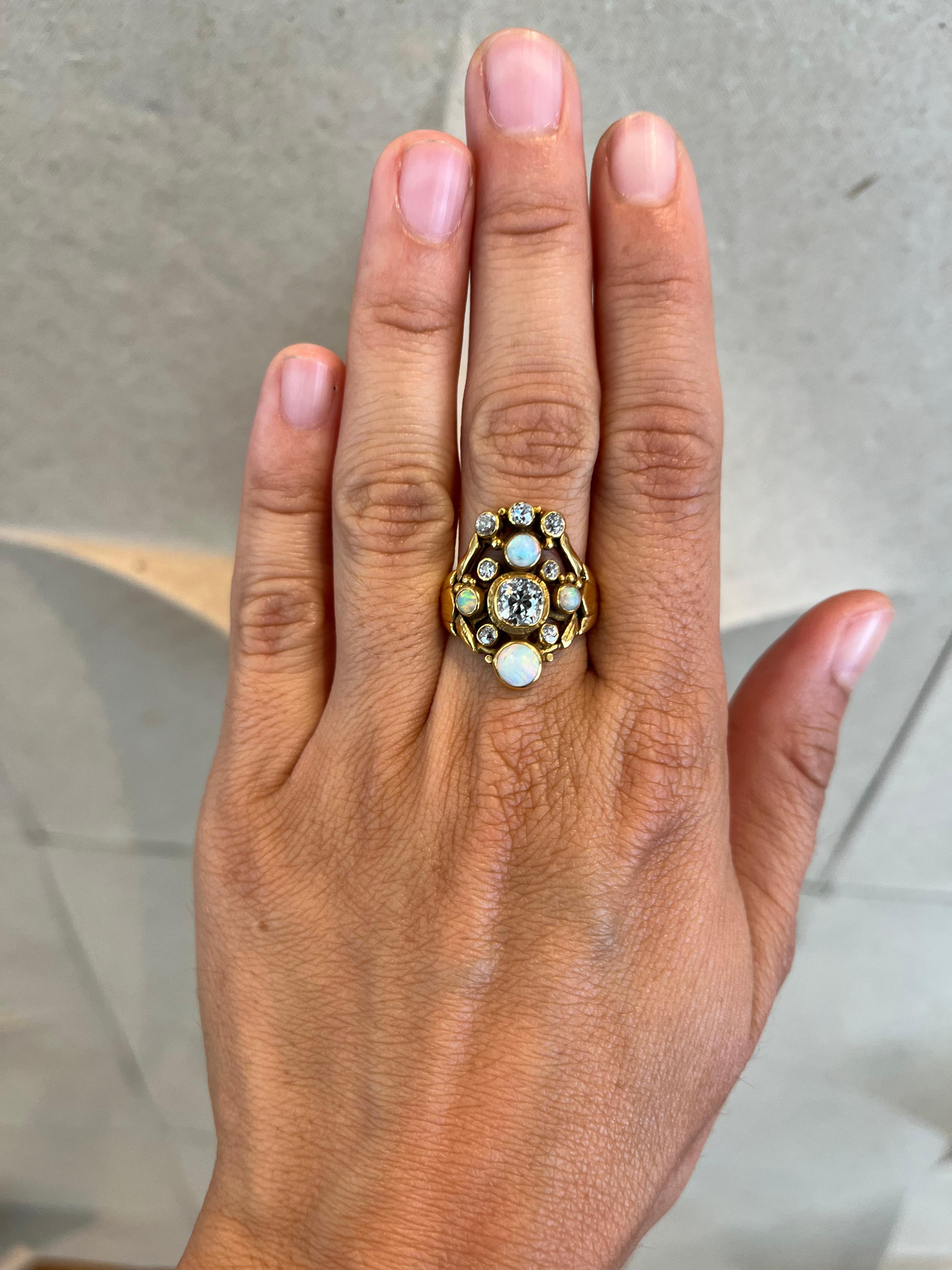 Questo straordinario anello in stile Art Nouveau del 1900 circa cattura la bellezza eterea dell'epoca con un'armoniosa miscela di diamanti antichi e opali luminosi. Al centro si trova uno splendido diamante da 0,80 carati (VS2, E-F), circondato da