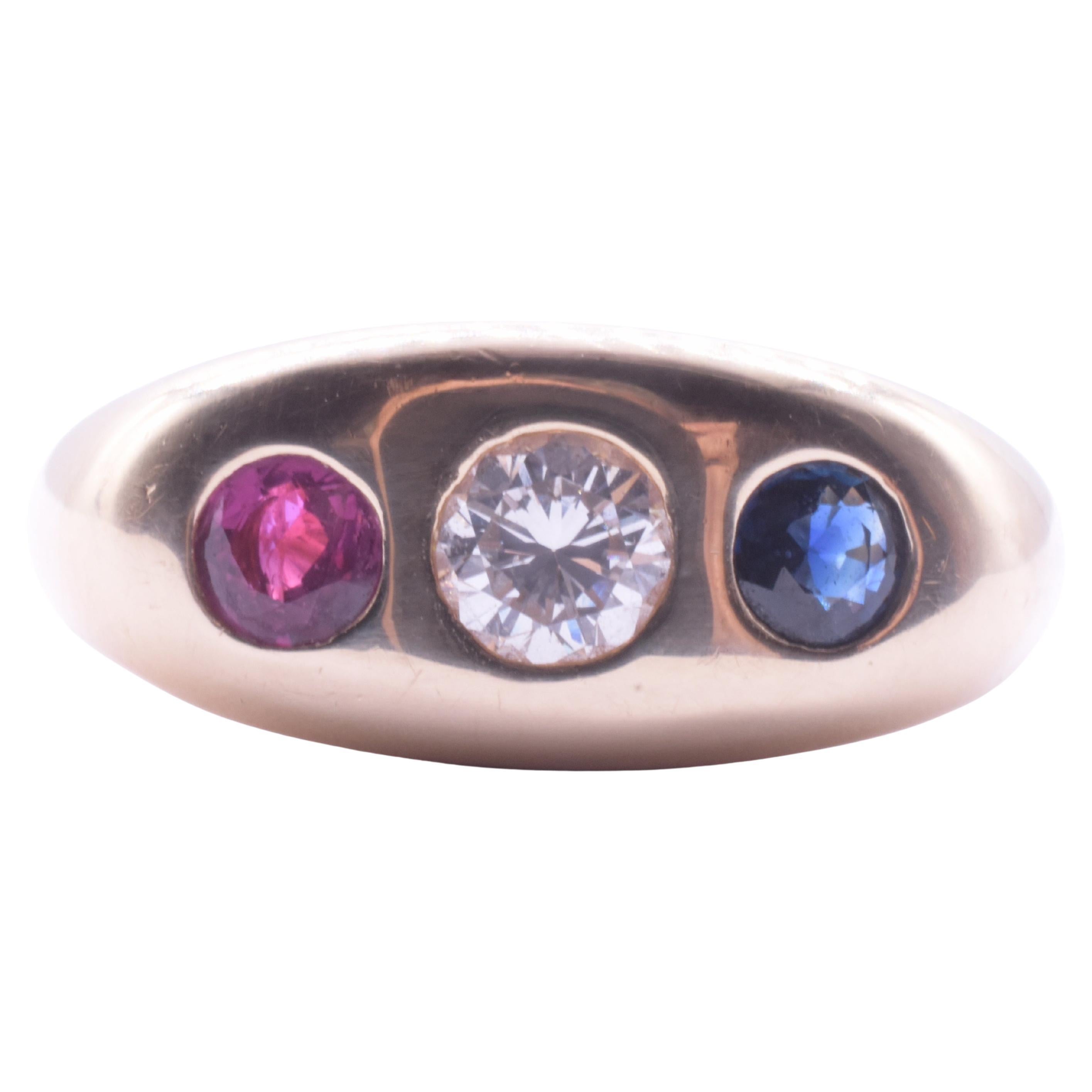 Nos encanta este anillo de tres piedras por su llamativo conjunto rojo, blanco y azul, que incluye un importante zafiro, un rubí y un diamante.  Nuestro anillo pesa 10 gramos. 
Los anillos de tres piedras con montura enrasada fueron populares desde