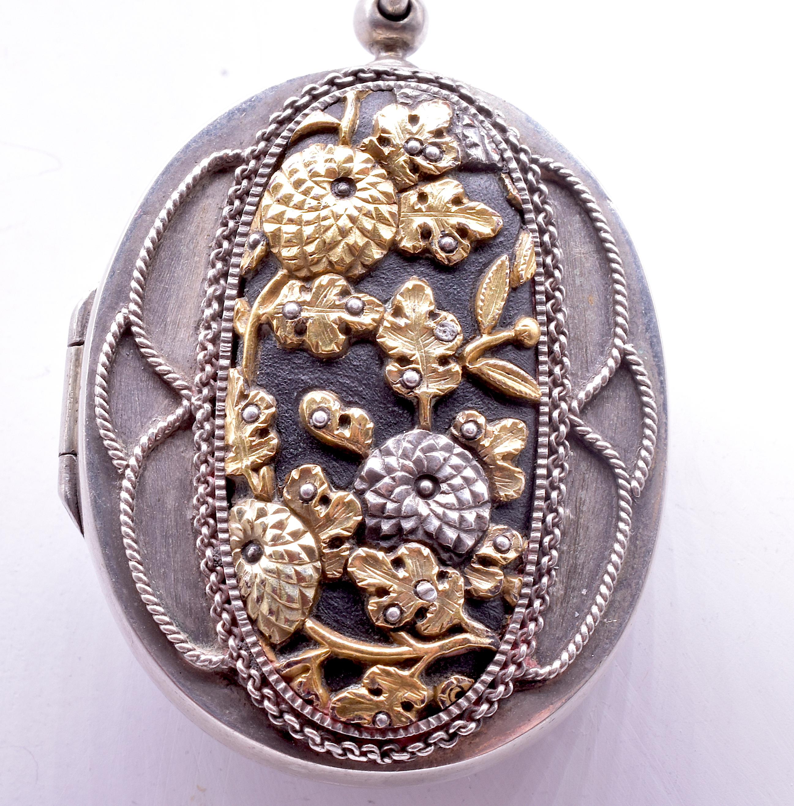 Stunning Shakudo necklace set on silver and inlaid with copper and gold. One side of the 2 sided locket shows a stylized scene of ornately carved leaves and chrysanthemums, a symbol of the Japanese monarchy. The other side shows two satirically