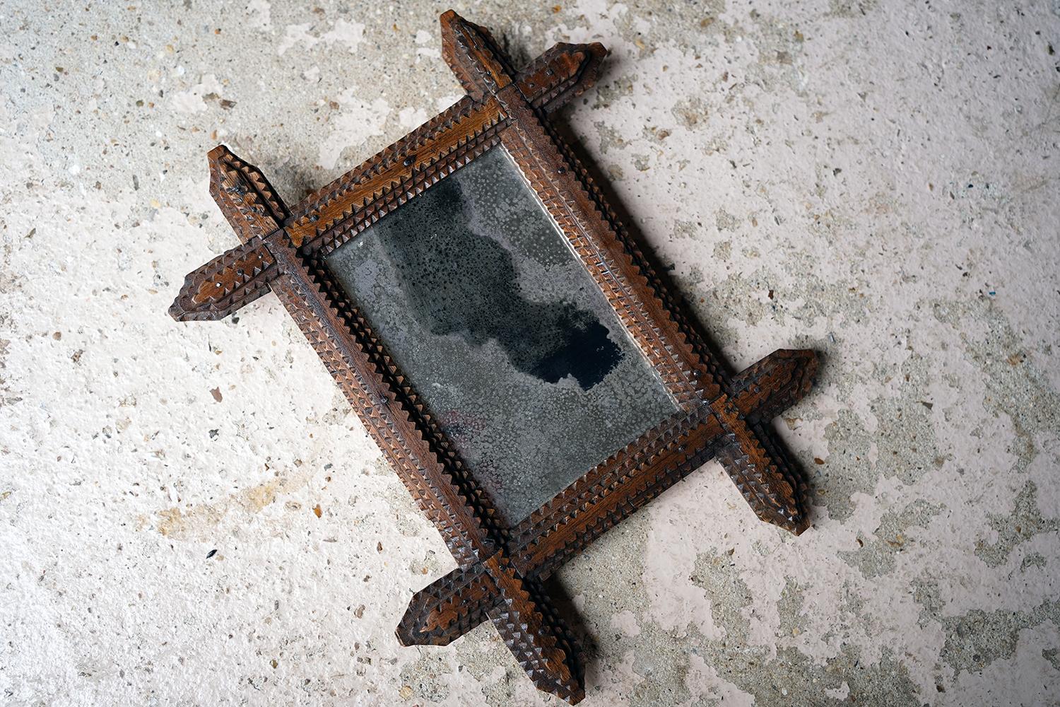 The small tramp art wall mirror, retaining the original foxed plate, within a geometrically chip and notch carved stained pine frame and surviving from the zeniths of the nineteenth century.

The mirror is in very attractive, original and
