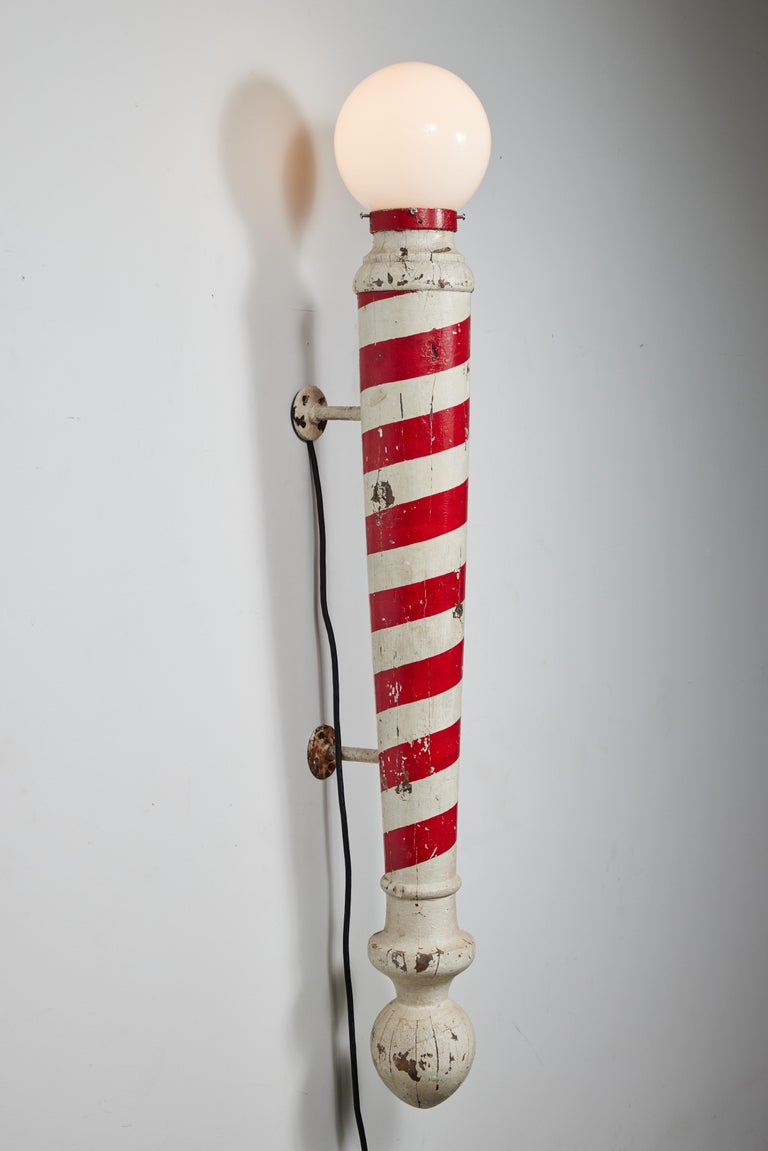 Great Americana! c. 1920s American Folk Art wood and iron carved barber pole. Layers of thick original red and white hand painted surface. Substantial iron mounts and iron strapping around neck of sconce. Unique wall sconce with a decent amount of