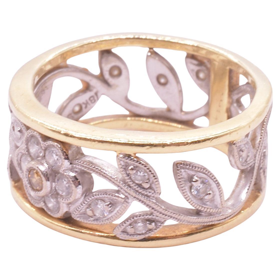Stylized 18 karat flower band with white and yellow gold accents, our ring has flower stems with carved leaves extending from the vertical gold strip on one side of the band and circling around in each direction to reach the flower 180 degrees