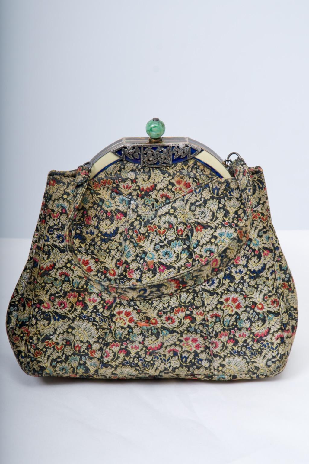 Borsa da sera in stile Art Déco, con il corpo realizzato in broccato a motivi floreali su sfondo nero e cucito. Degna di nota è la cornice e la chiusura in metallo dorato, la prima costruita con smalto color avorio sui lati e centrata su una base in