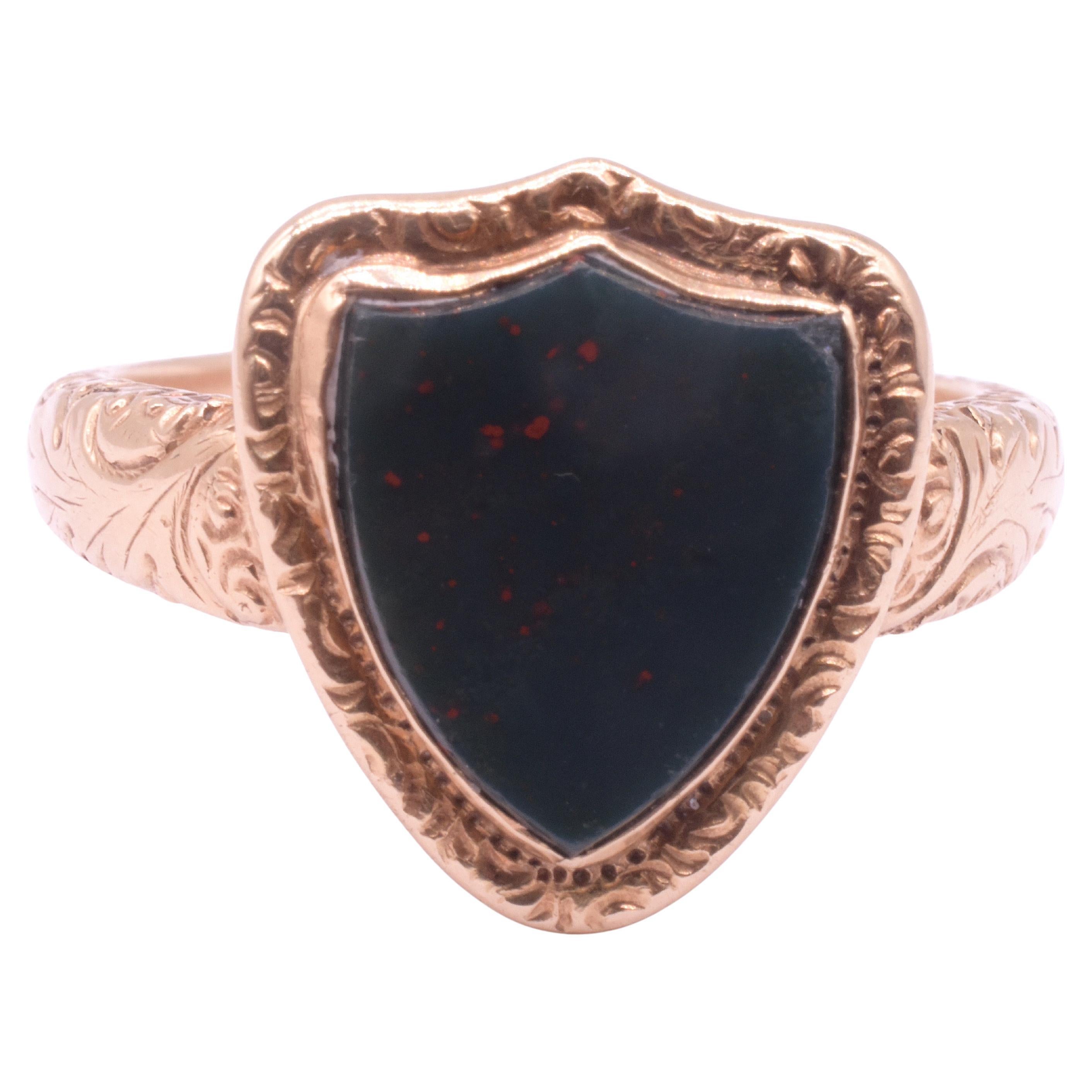 We love this bloodstone Chalcedony signet ring for its unusual decorative shield shape, a copy of a decorative shield that was popular in the 19th century. The shape of this escutcheon (another name for shield) is called 
