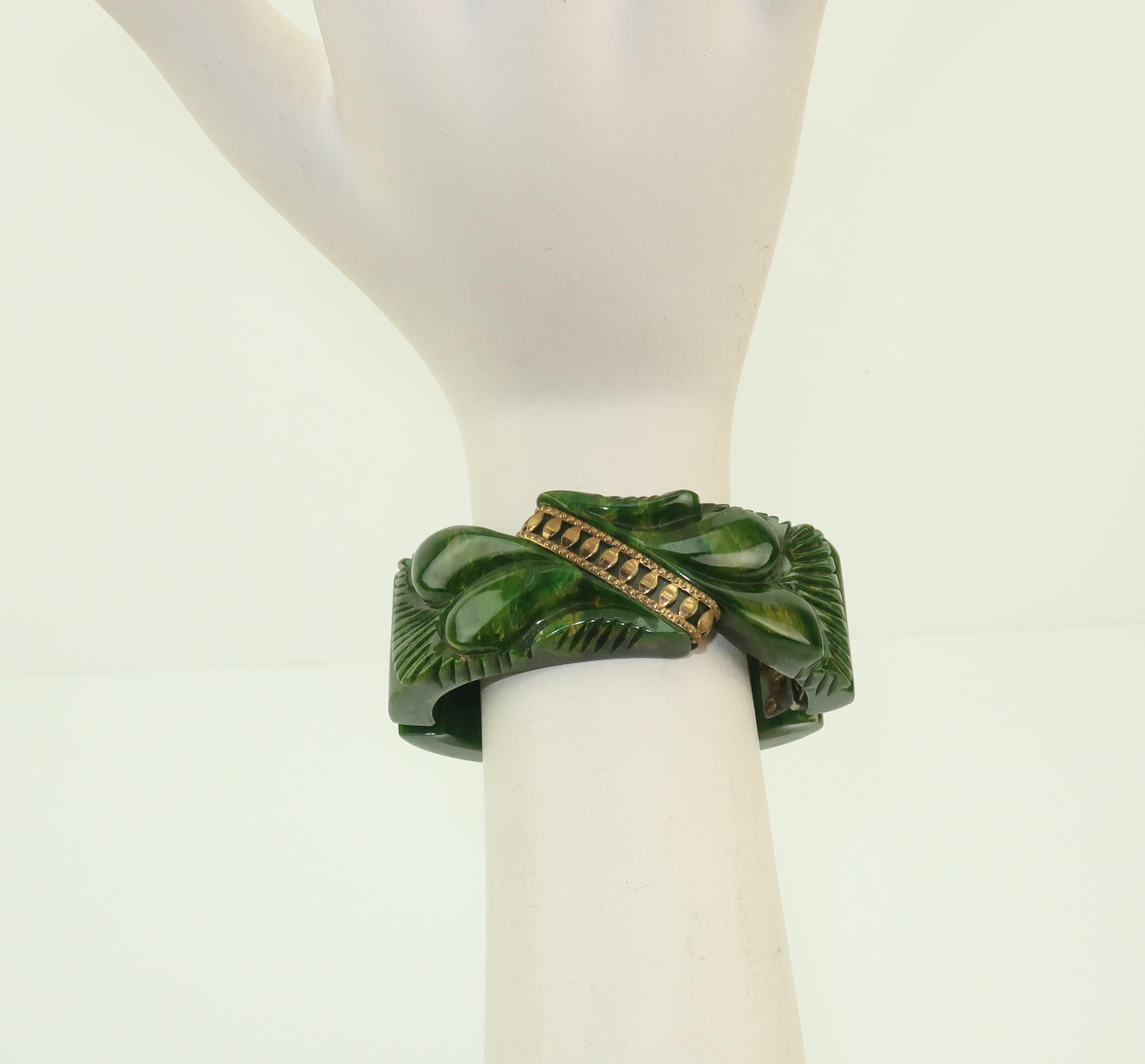 Glorious green!  A C.1940 marbled look green bakelite bracelet with an exotic carved motif accented with a gold tone detail.  The clamper style sports a hinge at the side and the oval silhouette gives the bracelet a fitted look perfect for