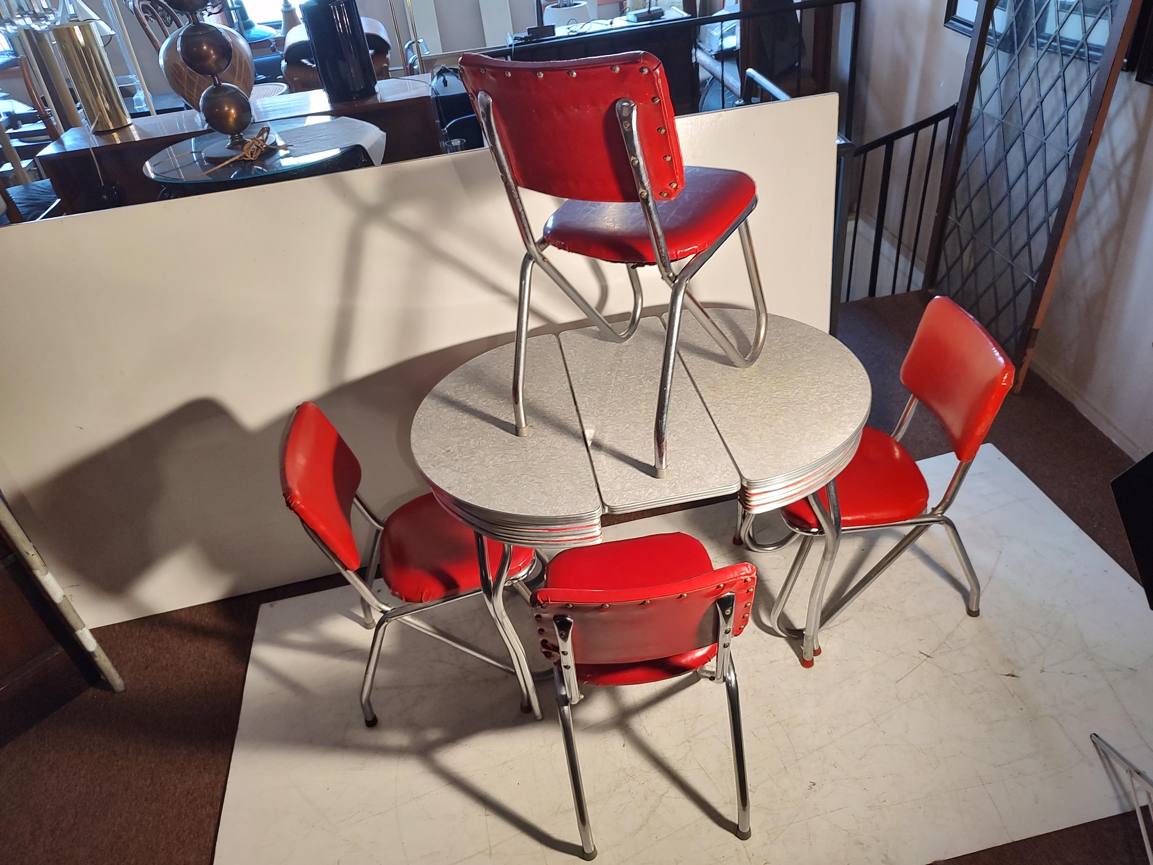 Diminutive table with one leaf to extend. 4 cherry red vinyl chairs with Sculptural legs for style, completely 1950. In very good condition with normal wear. See pics, one leg cap on the table missing. Ding on tabletop.