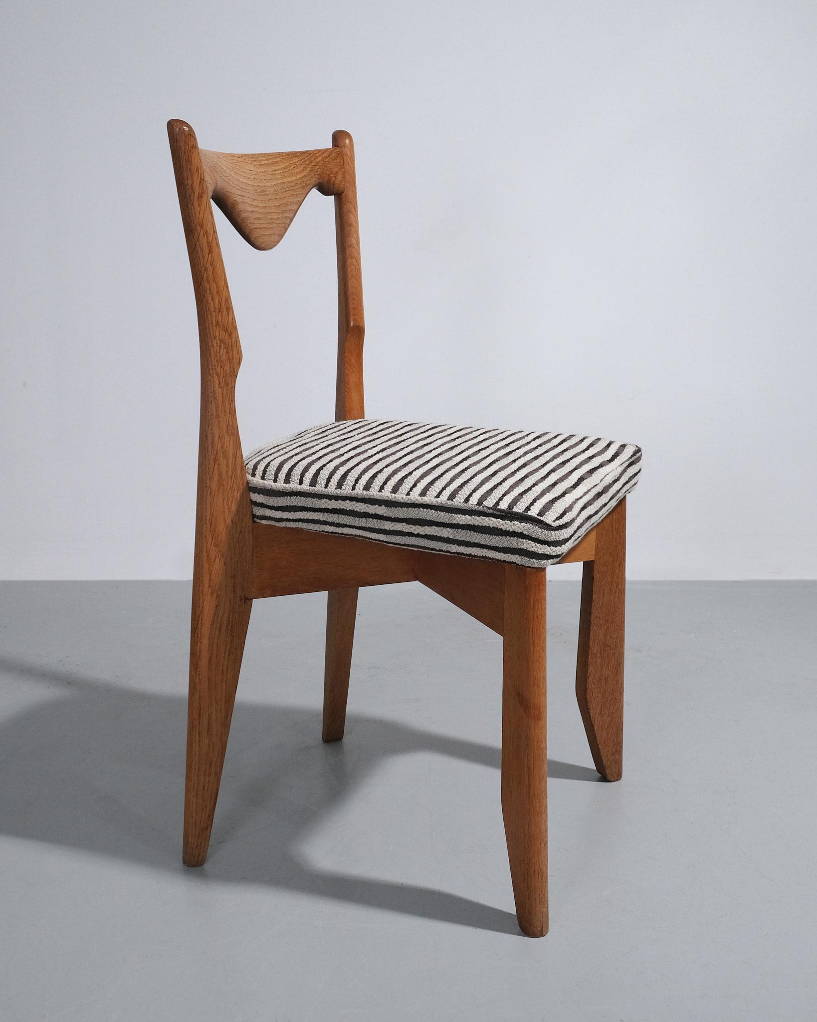 Cette paire de chaises de salle à manger, conçue par Guillerme et Chambron dans les années 1950, est fabriquée en chêne massif et revêtue du tissu California 10 de Tibor. Les chaises présentent des dossiers hauts et légèrement incurvés qui mettent