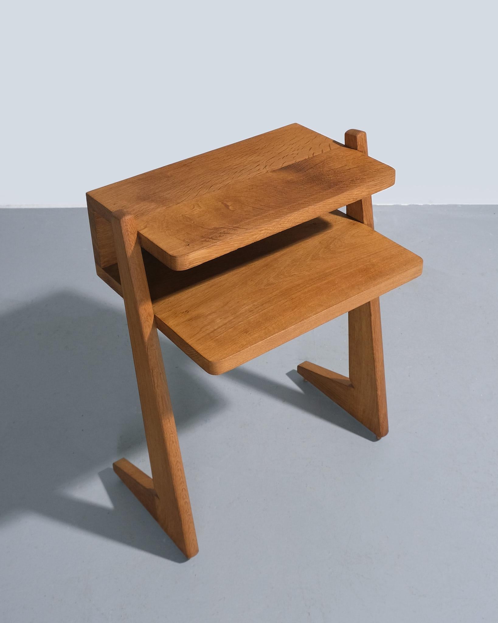 Cette table d'appoint à étagères de Guillerme et Chambron pour l'Edition Votre Maison, datant des années 1960, est réalisée en chêne ciré. Compact, le design présente une surface supérieure rectangulaire au-dessus d'une étagère ouverte, offrant de