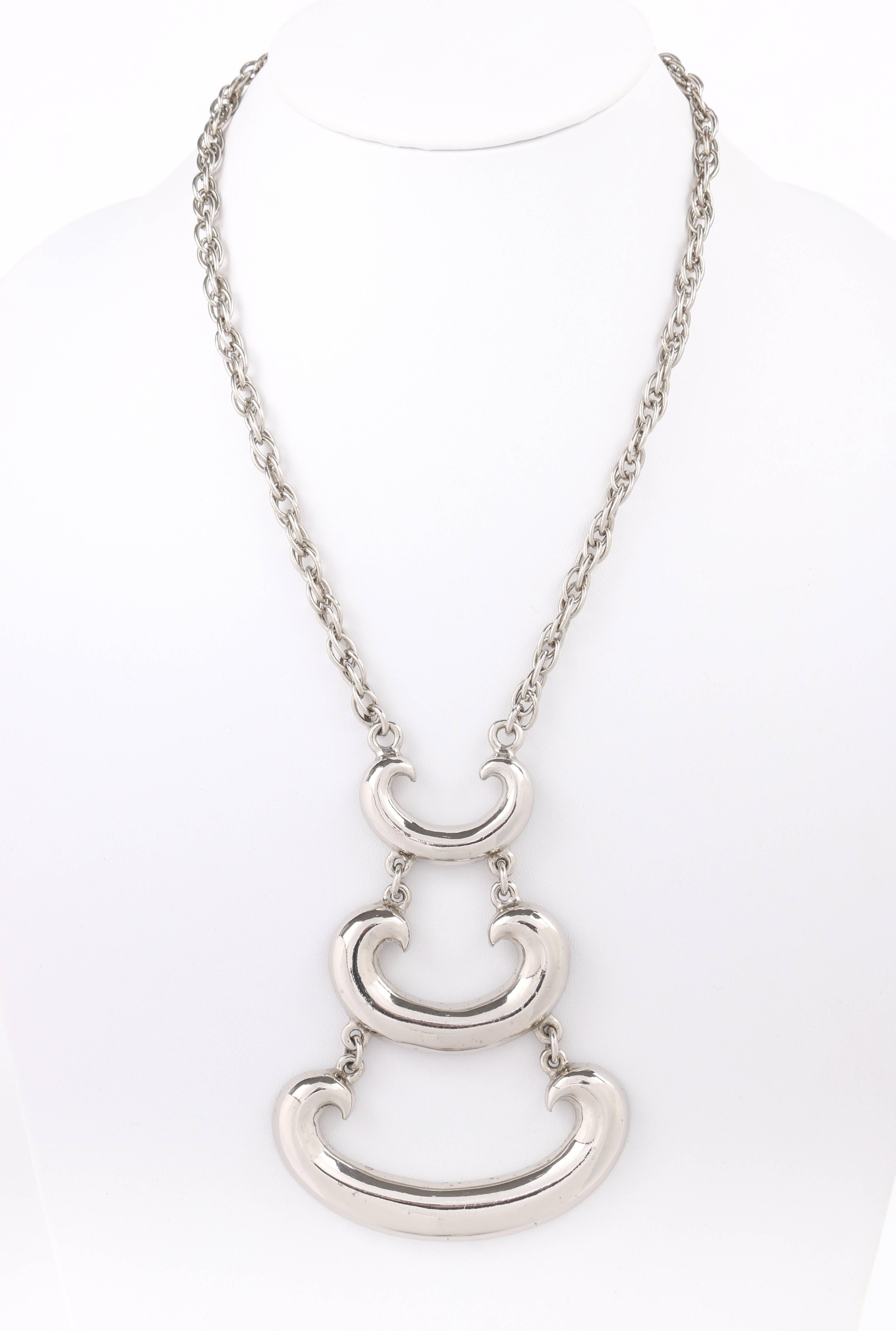 Vintage c.1960's silver modernist tiered pendant statement necklace. Large modernist pendant made up of three polished silver-toned metal curved shapes in varying sizes. Each tier is suspended by two o-rings. Pendant is suspended from a silver-toned
