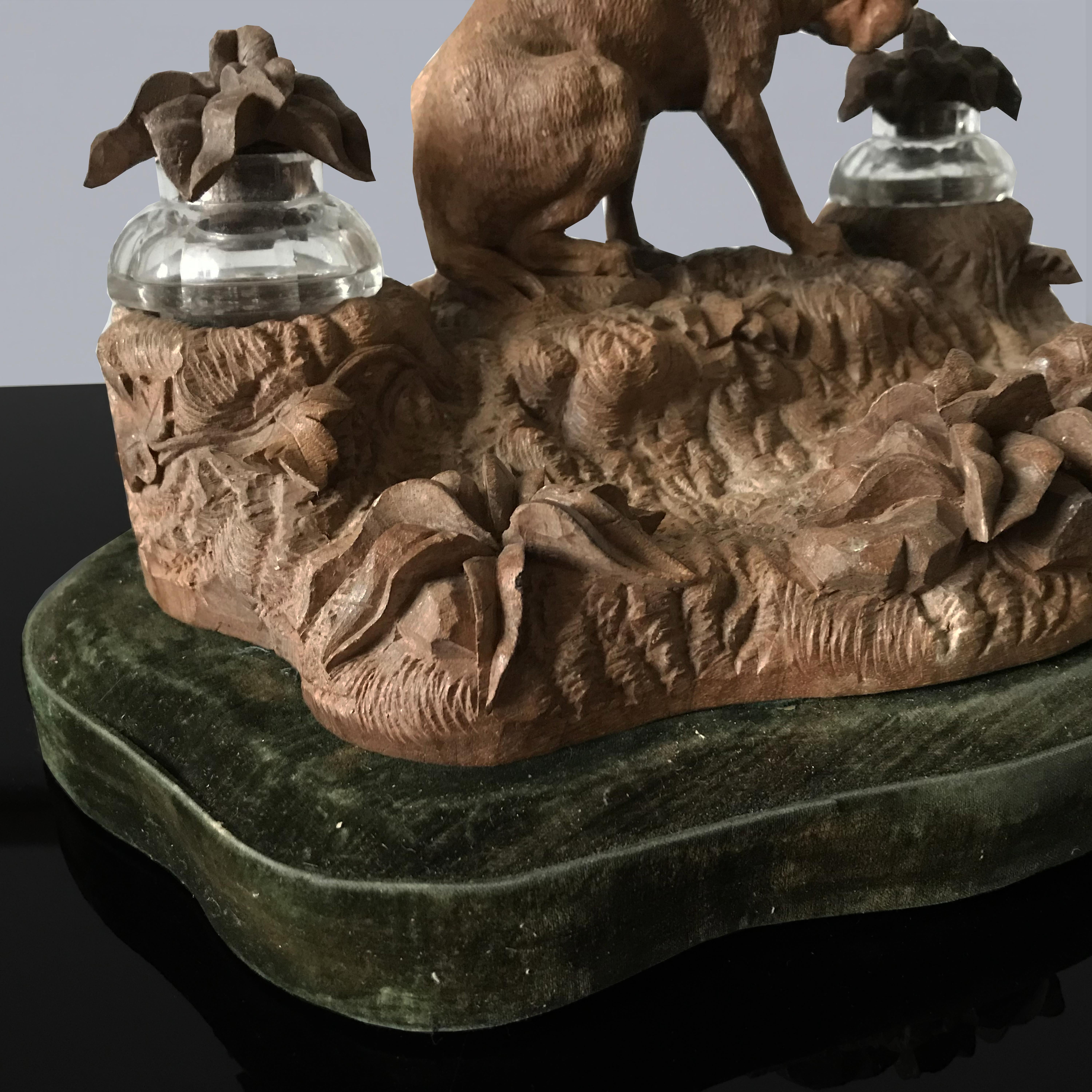 Wonderful German late 19th century carved wood black Forest inkwell. Beautifully carved with a seated dog on a naturalistic base of ferns and foliage, the cut glass inkwells retaining their original leaf carved stoppers, the shaped base covered in