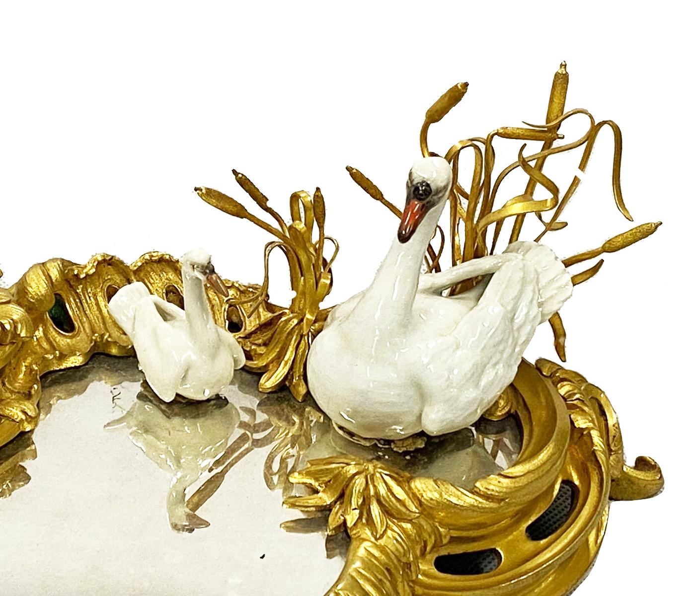 A fine quality late 19th century gilded ormolu Ink well, in the Rococo style, having a hinged lid, a mirrored faux pond with a porcelain Swan and cygnet among reeds. In the manner of Meissen.