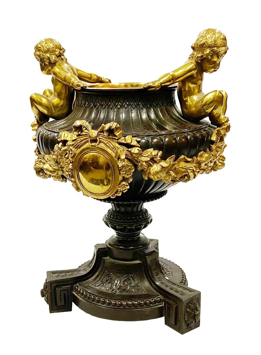 A classical 19th century French bronze urn, having wonderful gilded putti seated on either side, with garlands of flowers hanging from a central pendant, raised on a pedestal base with beeded and motif mounts. Measures: 9.5